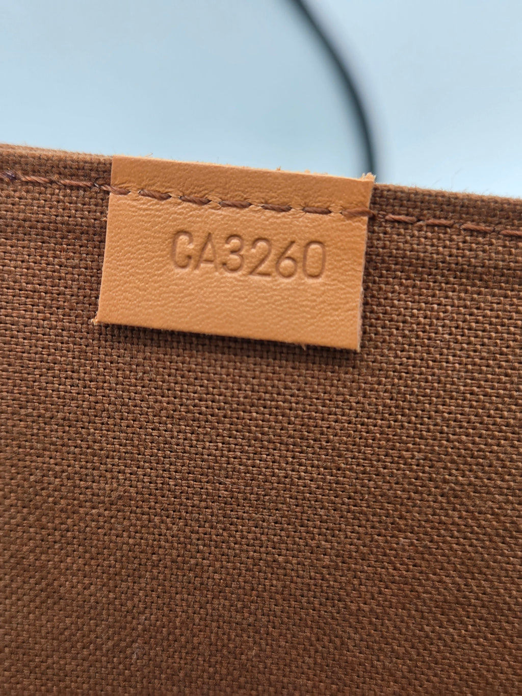Close-up of a brown woven fabric surface with a small tan leather tag stitched onto the edge, embossed with the text CA3260.
