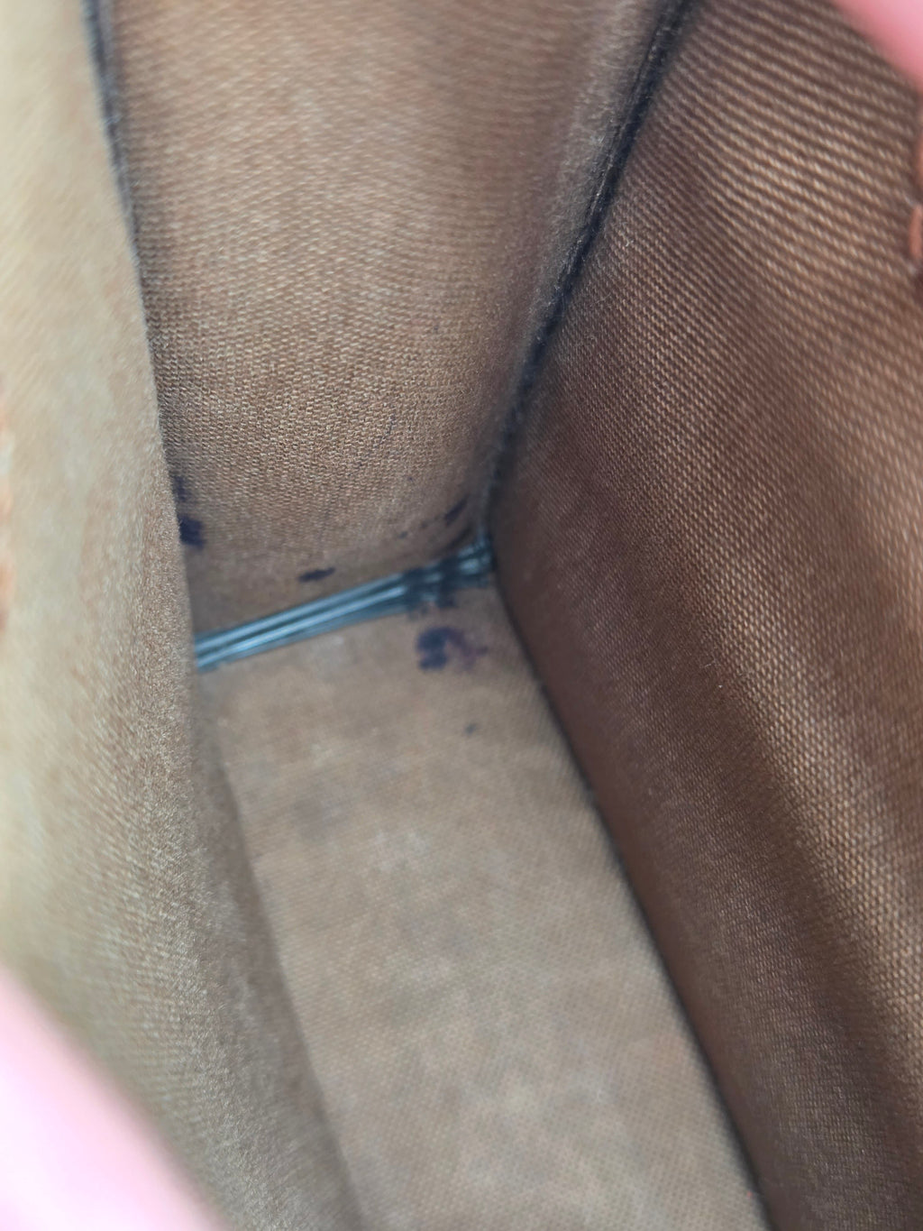 Close-up of the interior corner of a brown canvas or fabric bag, showing the woven texture and a small metal zipper pull.