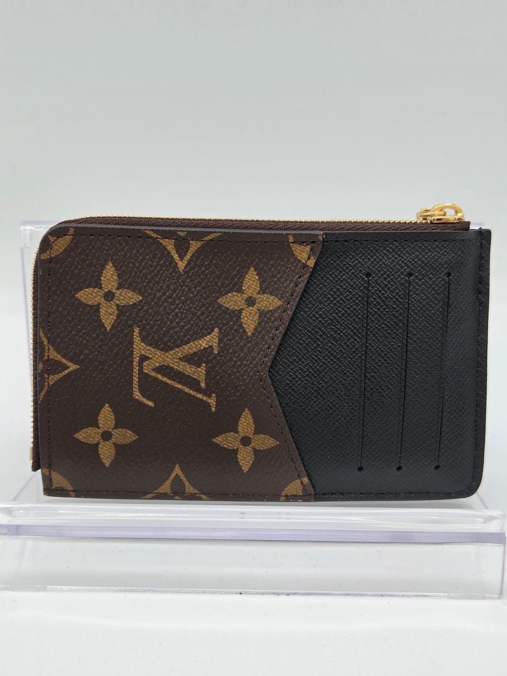 Louis Vuitton monogram canvas zip-around card holder wallet in brown and black, shown inside a clear plastic display case against a light gray background.