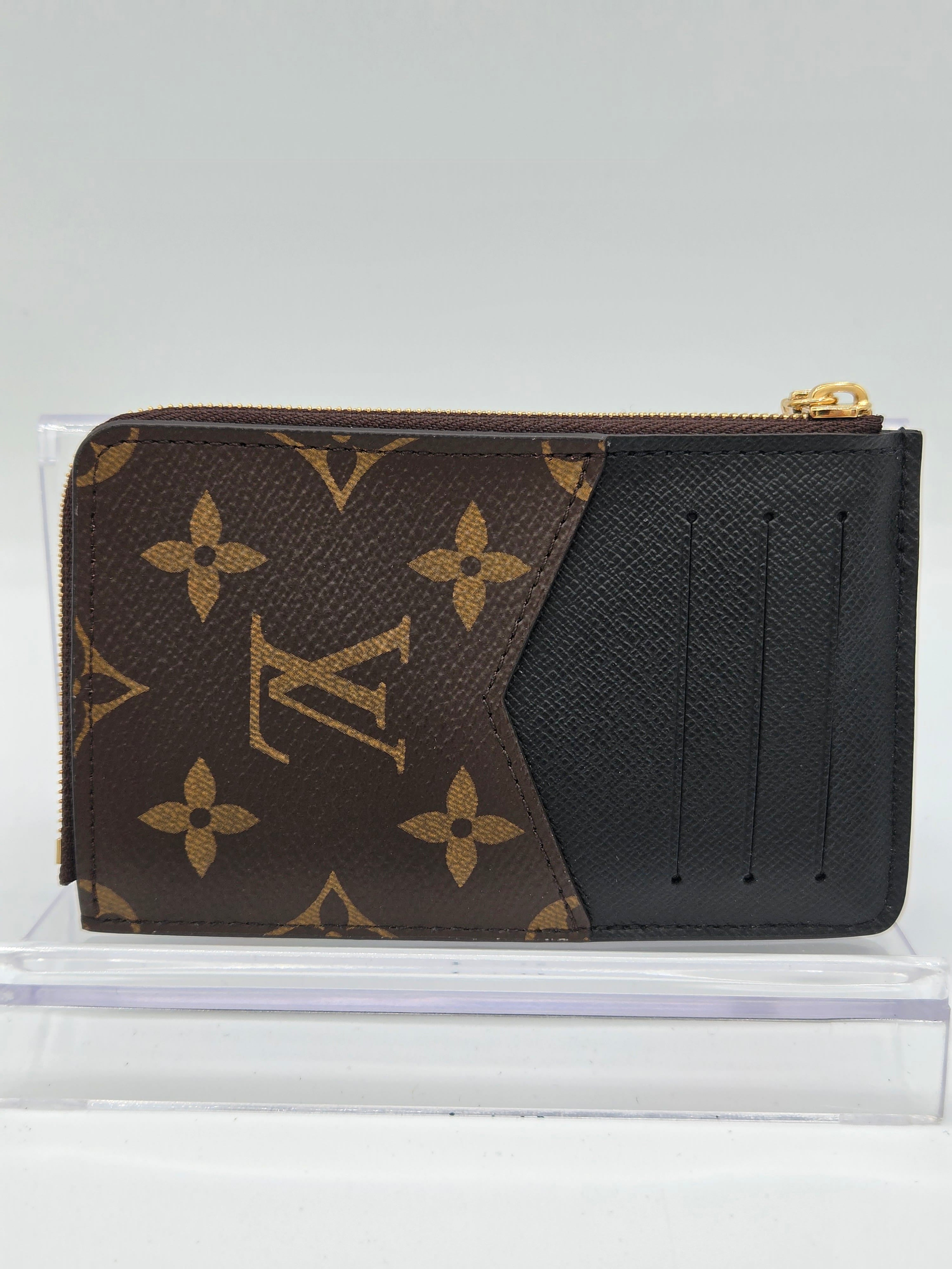 Louis Vuitton monogram canvas zip-around card holder wallet in brown and black, shown inside a clear plastic display case against a light gray background.