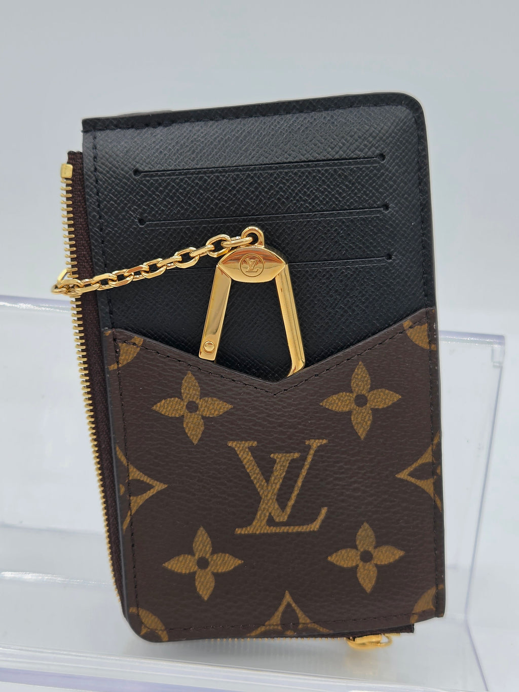 A Louis Vuitton monogram card holder wallet in brown and black with gold-tone hardware and a chain detail, displayed against a light gray background.
