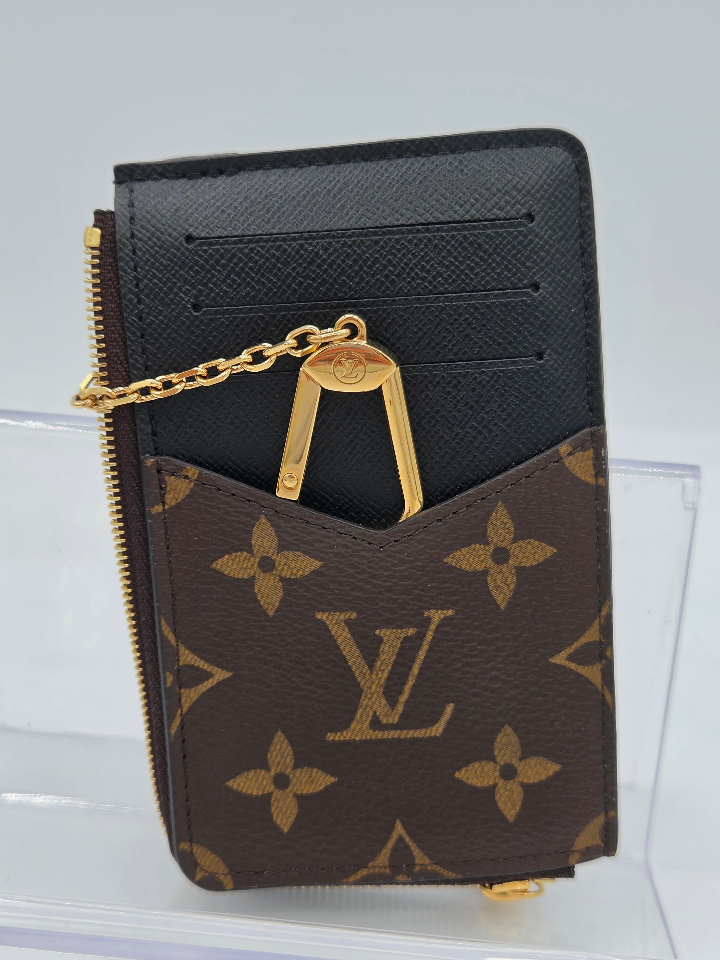 A Louis Vuitton monogram card holder wallet in brown and black with gold-tone hardware and a chain detail, displayed against a light gray background.