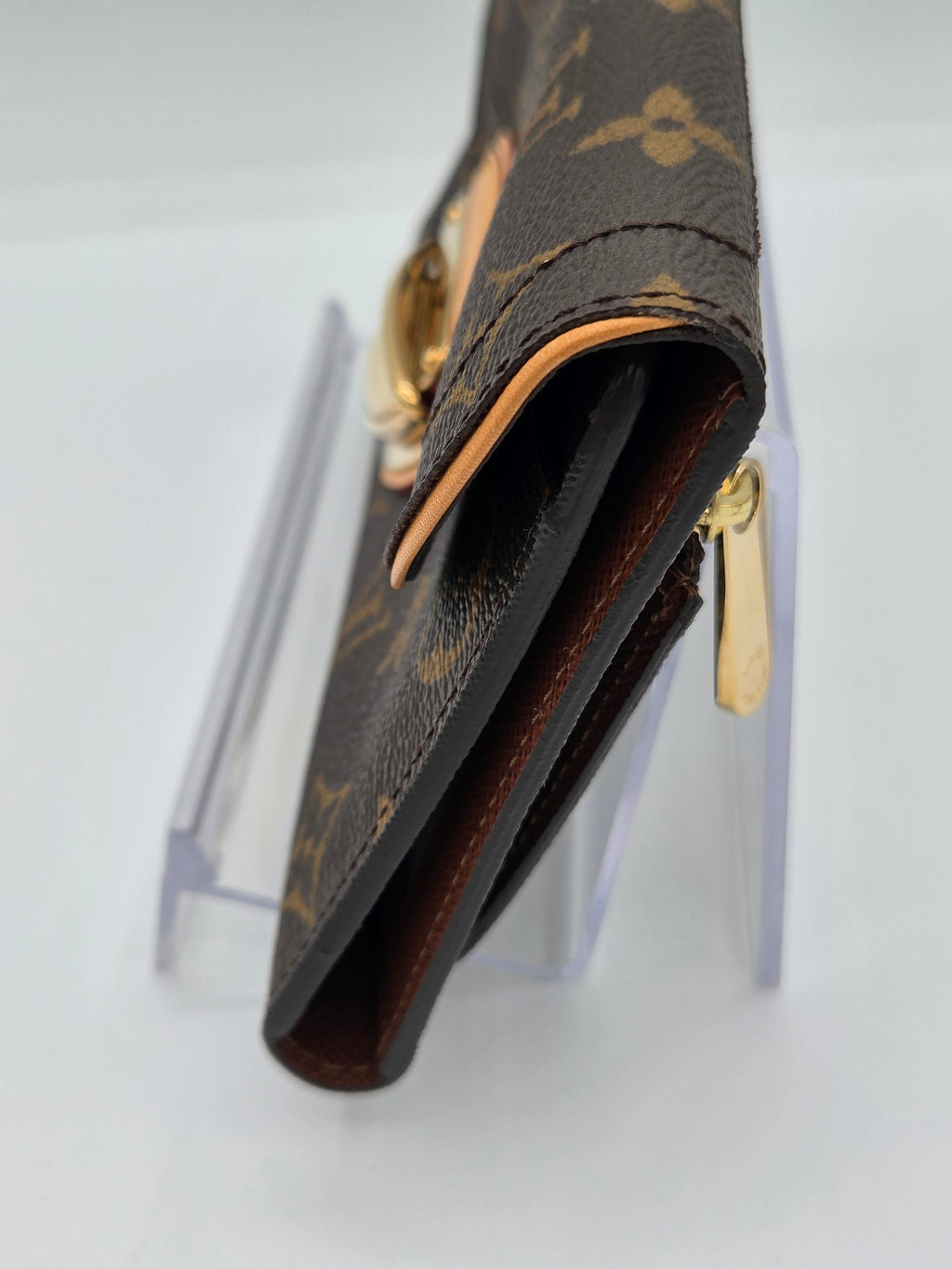A close-up of a Louis Vuitton monogram wallet or card holder in brown coated canvas with gold-tone hardware, mounted on a clear display stand against a white background.