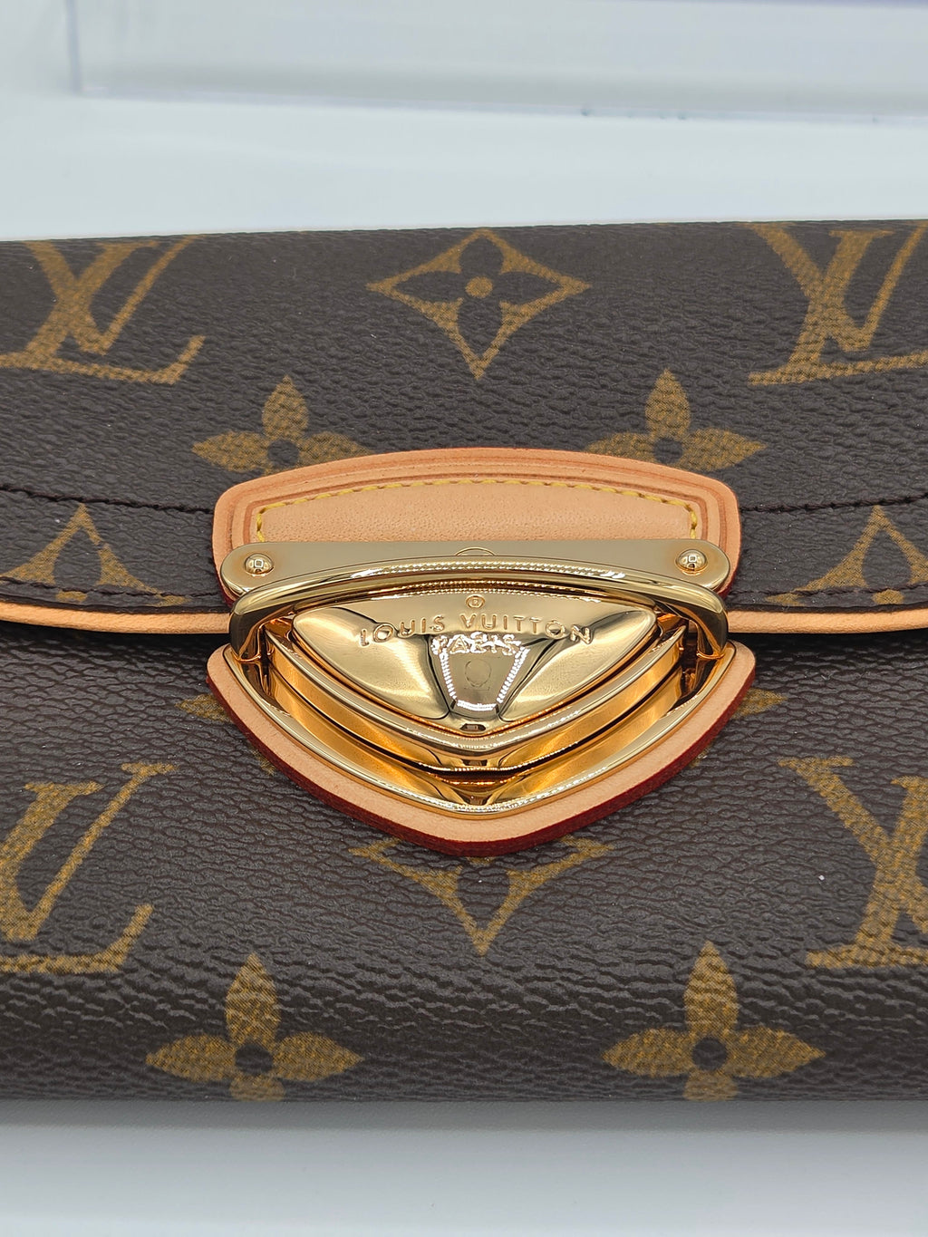 Close-up of a Louis Vuitton monogram bag featuring the iconic brown canvas with gold LV logos and a prominent gold-tone metal clasp with light tan leather trim.