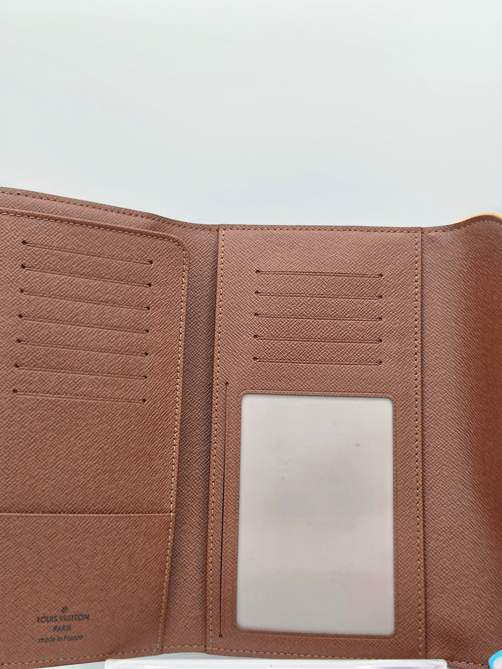 An open brown textured leather wallet or passport cover with multiple card slots and a clear ID window, photographed against a plain light background.