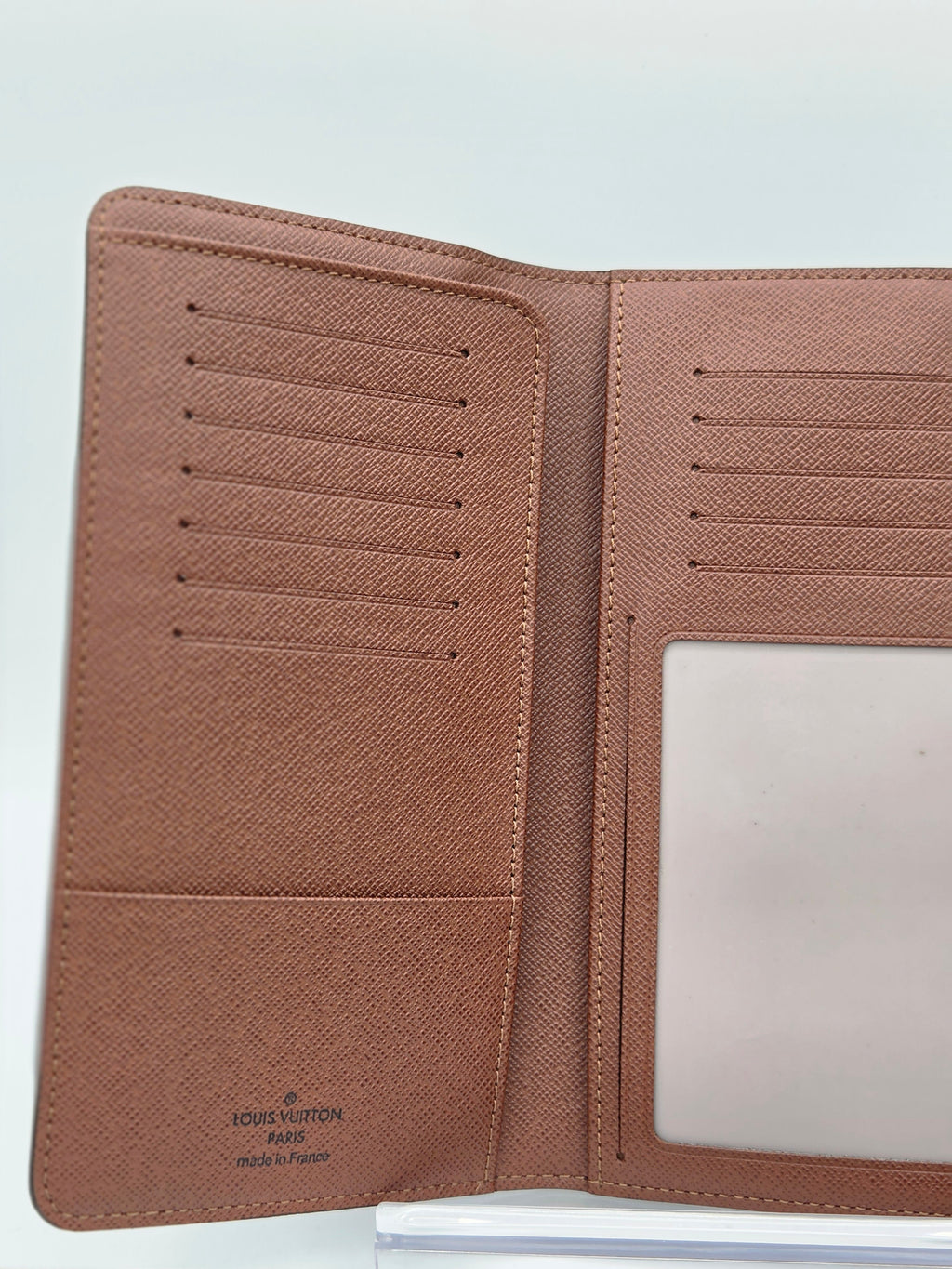 An open Louis Vuitton bi-fold wallet in brown textured leather, showing multiple card slots, a slip pocket, and an ID window on a light gray background.