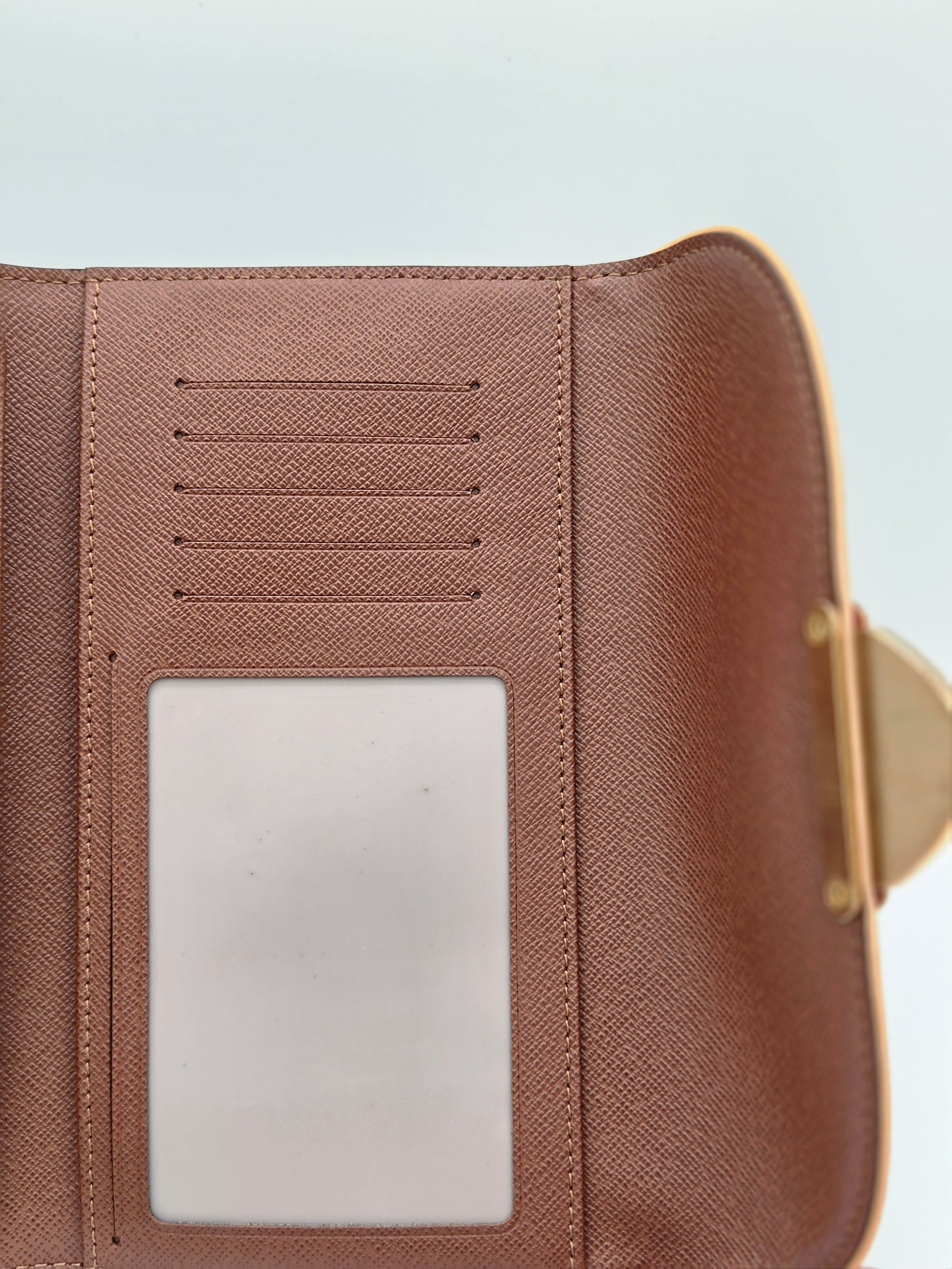 Close-up of a brown textured wallet interior showing card slots and a clear ID window, with a small gold-tone clasp visible on the right side against a pale blue background.