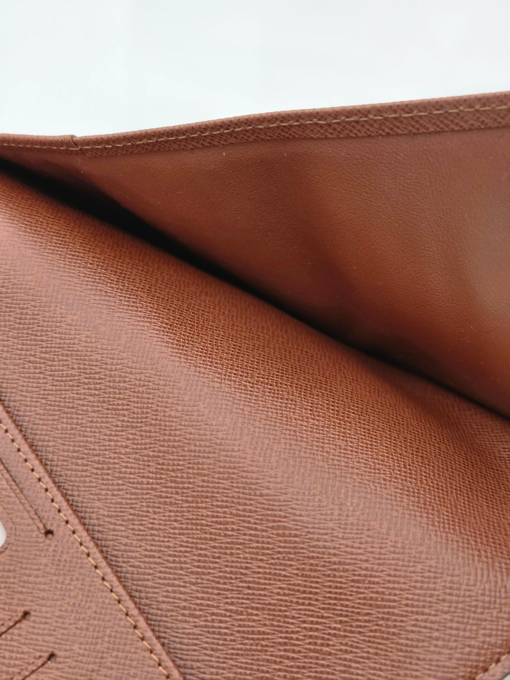 Close-up of a brown textured leather or faux-leather material with visible grain and stitching, shown against a white background.