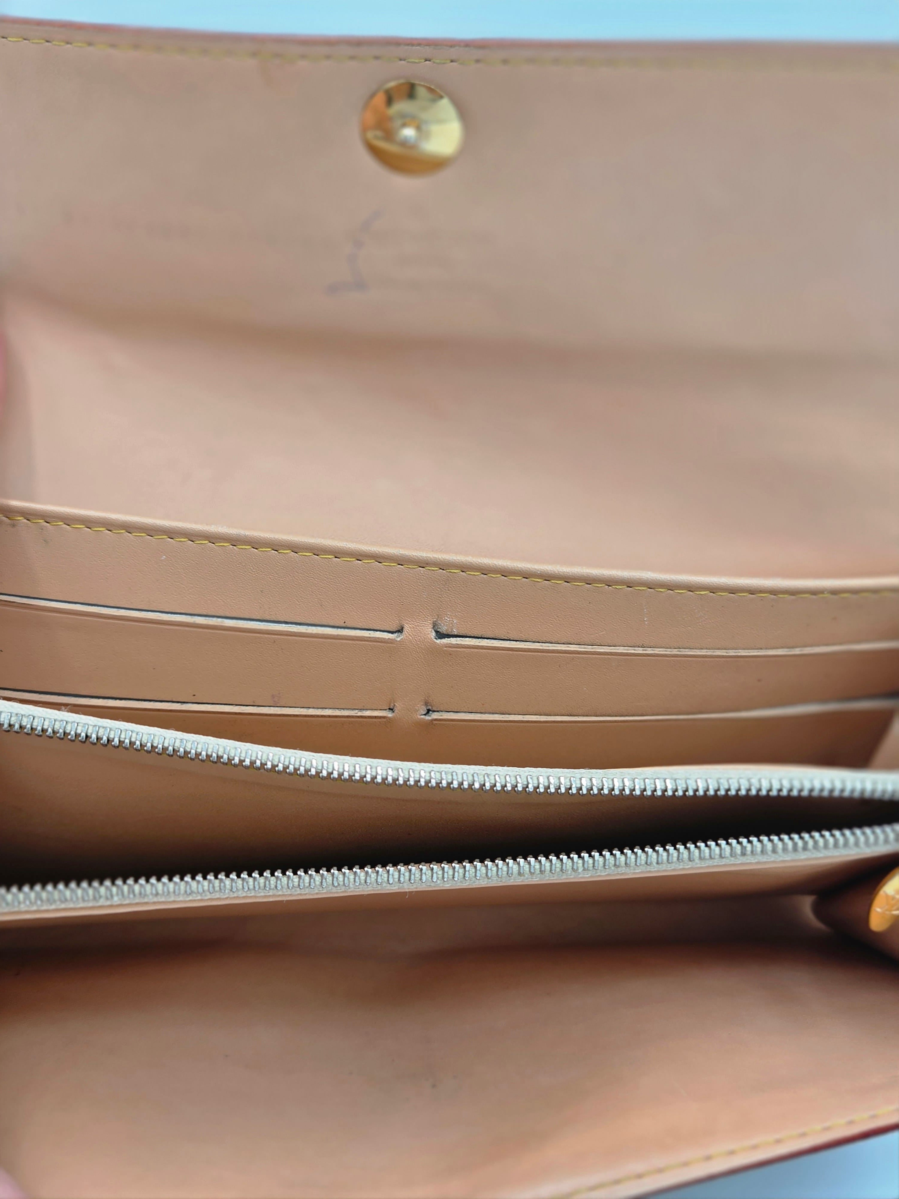 Close-up of the interior of a beige leather clutch or wallet, showing a gold snap button, interior card slots, and a silver zipper.