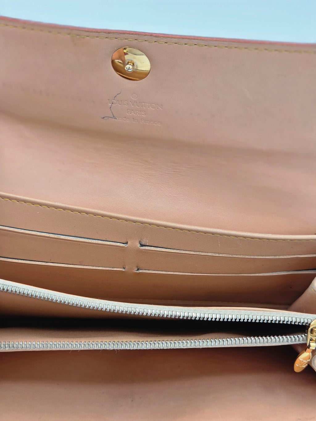 Close-up of a beige leather handbag interior showing a gold snap button, card slots, and a silver zipper.