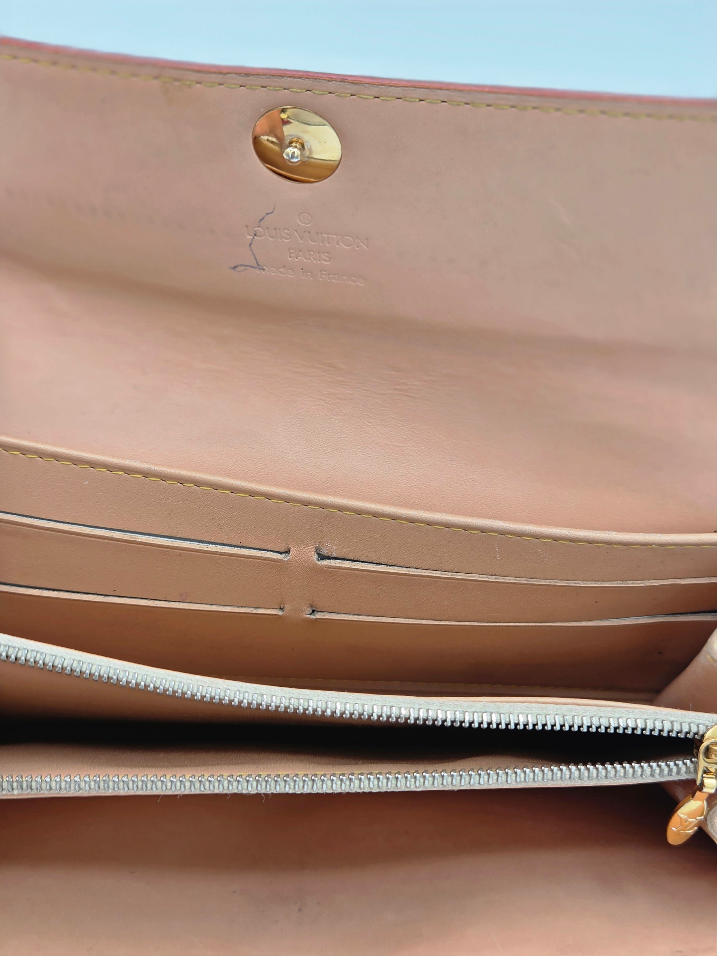 Close-up of a beige leather handbag interior showing a gold snap button, card slots, and a silver zipper.