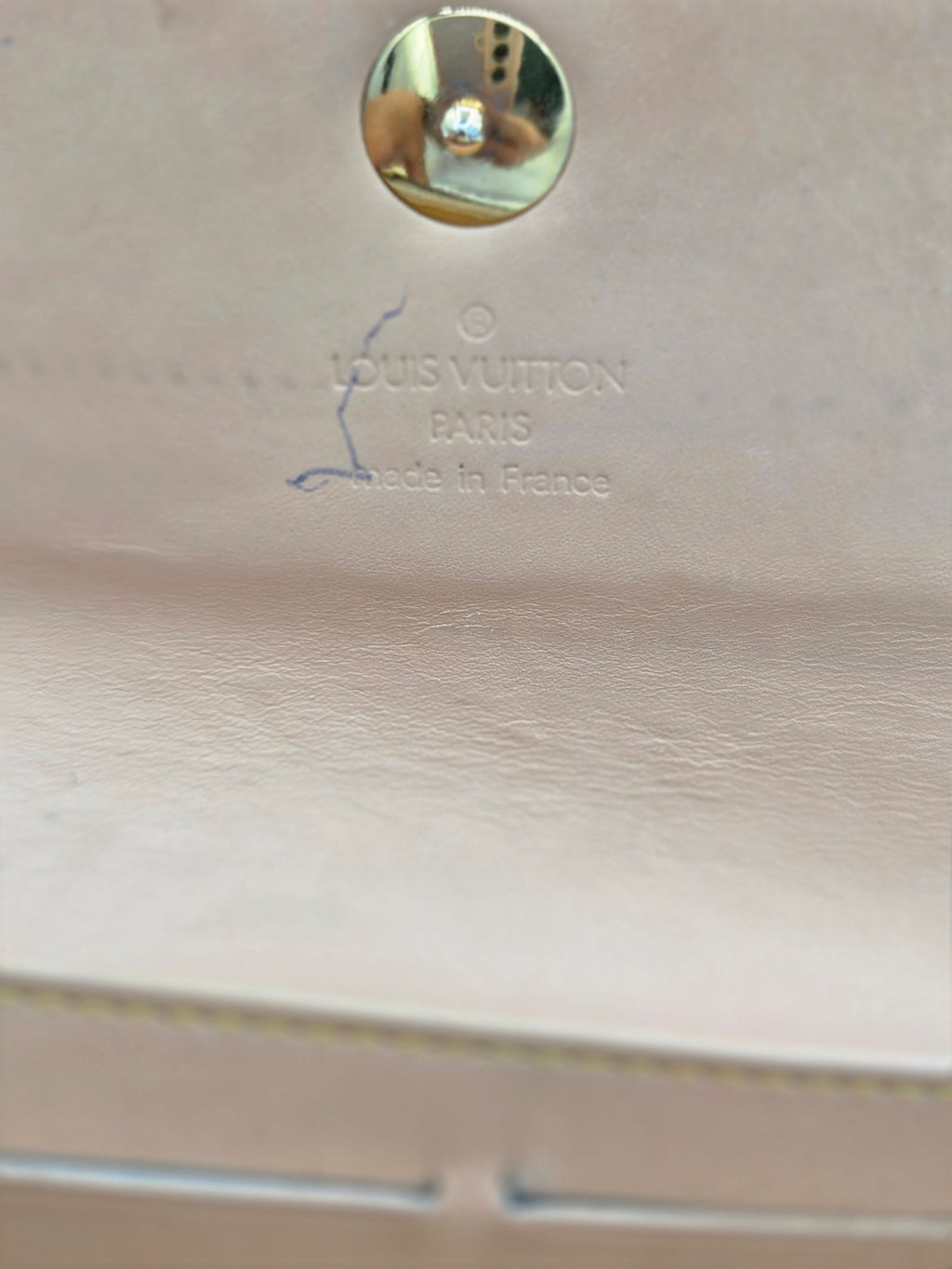 Close-up of a light beige leather Louis Vuitton bag showing the 'LOUIS VUITTON MADE IN FRANCE' stamp and a round metal stud closure.