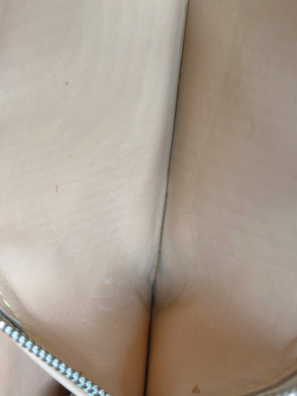 Close-up of the interior lining of a beige or light tan bag, showing a smooth leather or faux-leather surface with a silver zipper along the top edge.