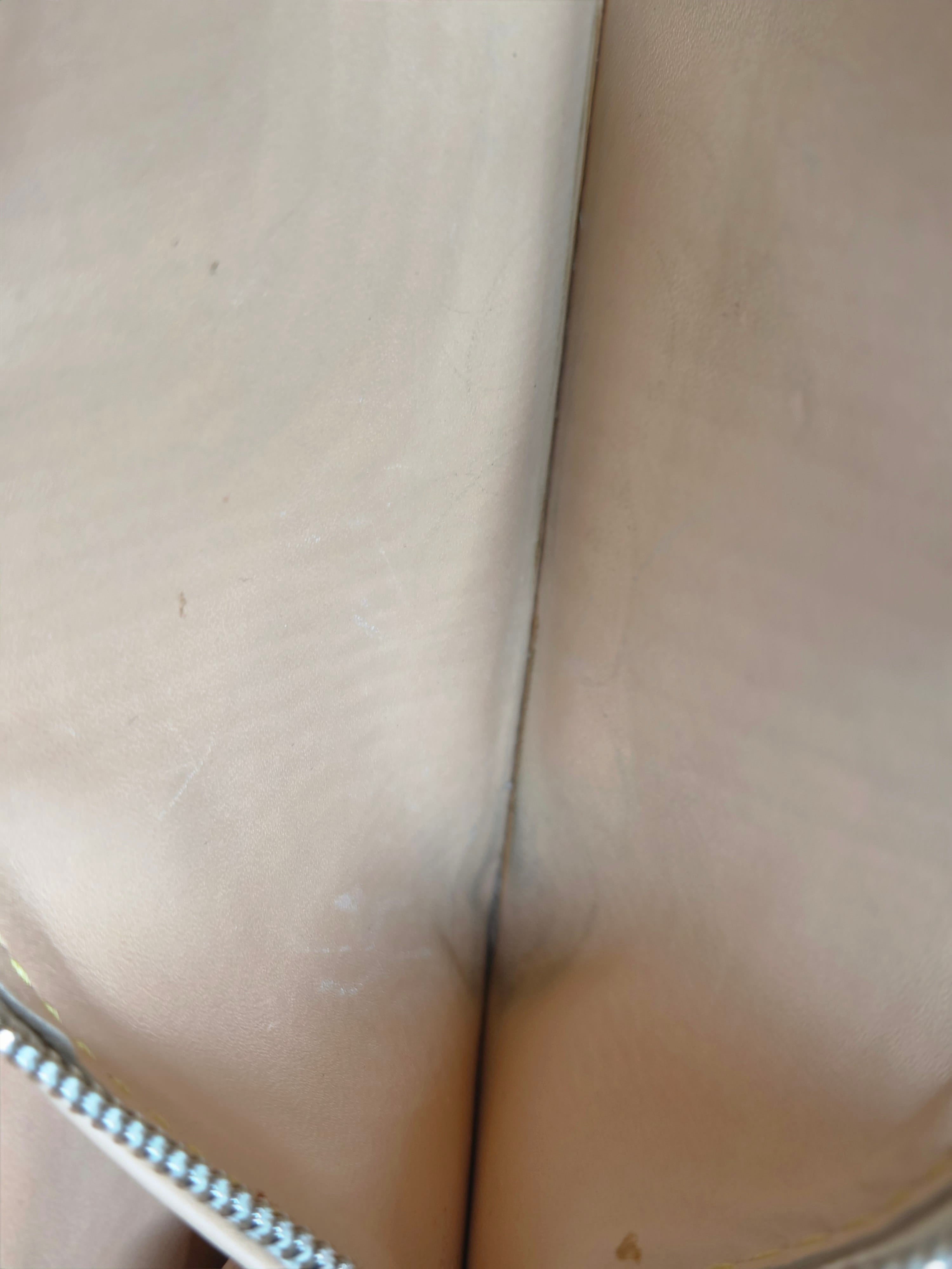 Close-up of the interior lining of a beige or light tan bag, showing a smooth leather or faux-leather surface with a silver zipper along the top edge.