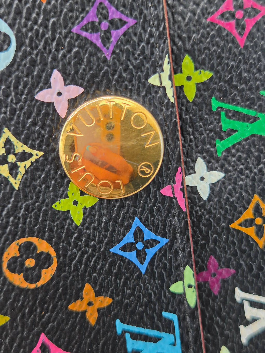 Close-up of a Louis Vuitton coin resting on a black textured leather surface decorated with colorful monogram flower motifs.