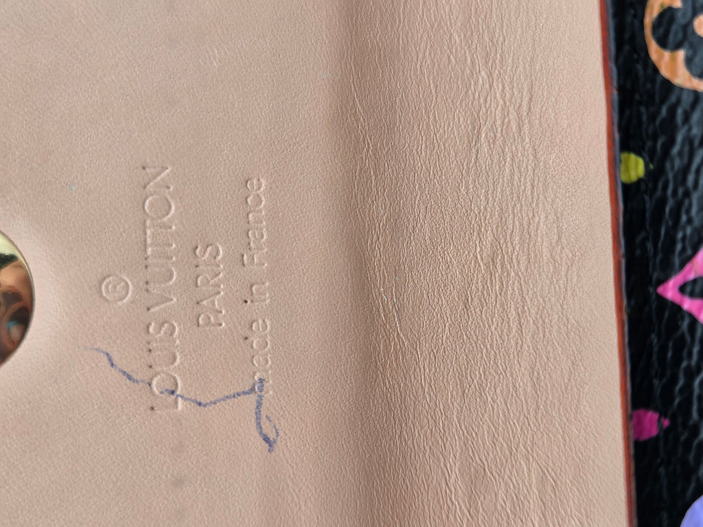Close-up of a beige textured leather interior with embossed Louis Vuitton Paris text and a small blue mark, next to a dark patterned surface with colorful accents.