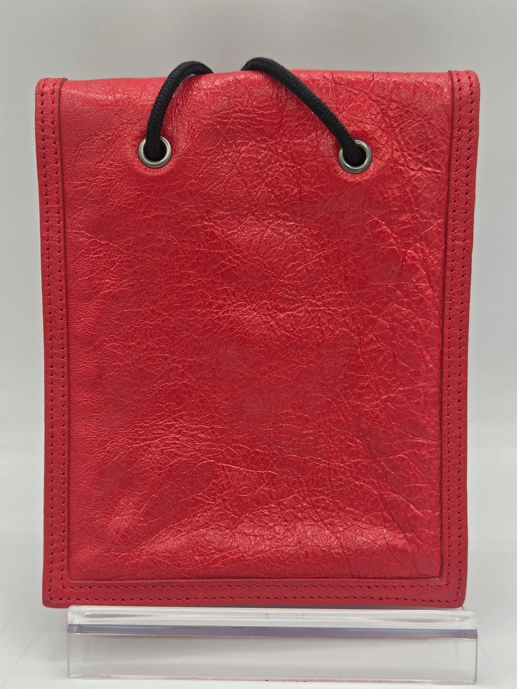 A red faux-leather binder cover with a black elastic loop and metal grommets, shown on a white background next to a clear plastic sleeve.
