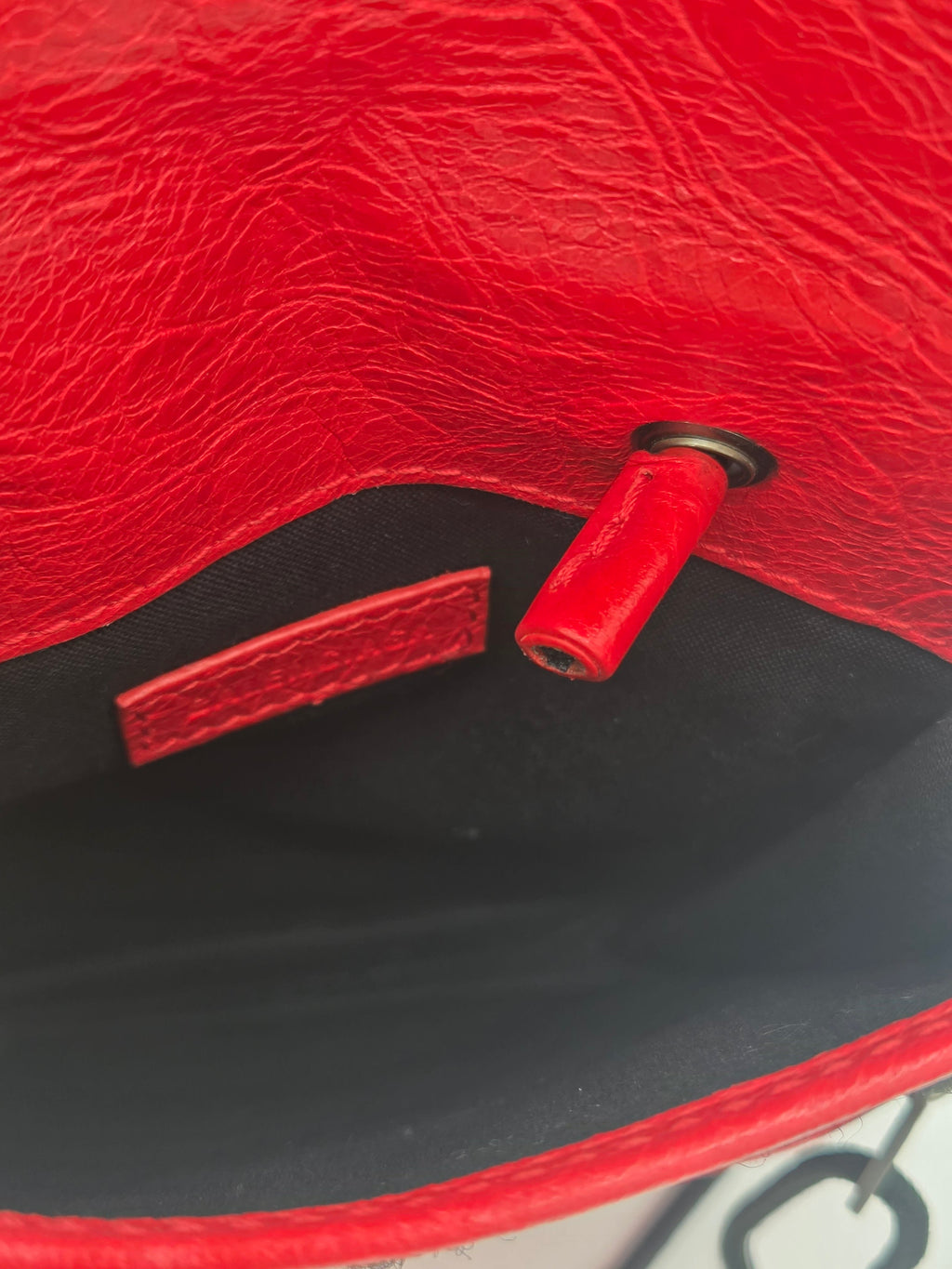 Close-up detail of a red textured leather bag showing the interior lining, a red leather pull tab, and a black metal eyelet.