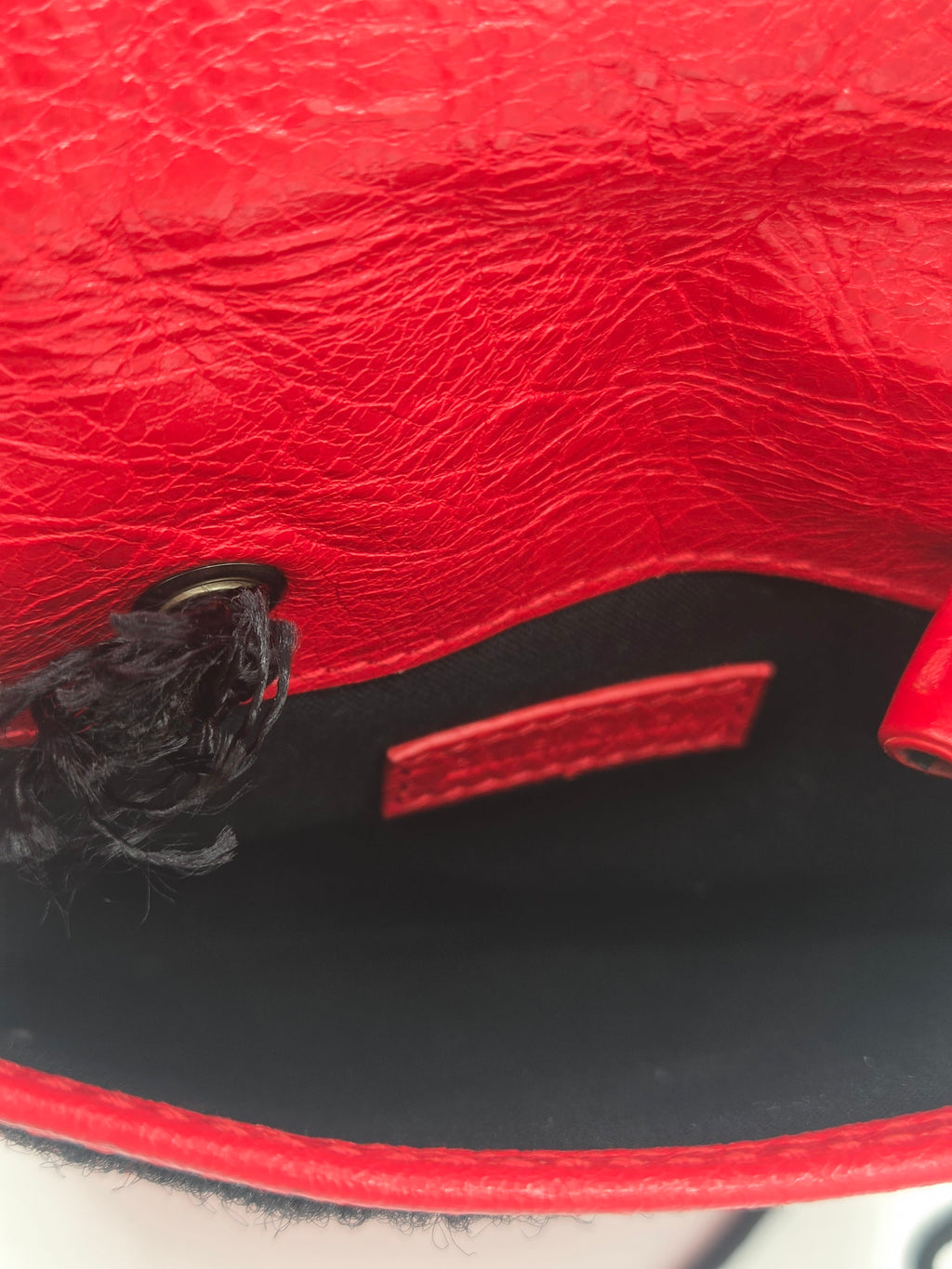 Close-up of a textured red leather bag interior with a black lining, a small red interior label, and a black tassel near a metal ring.