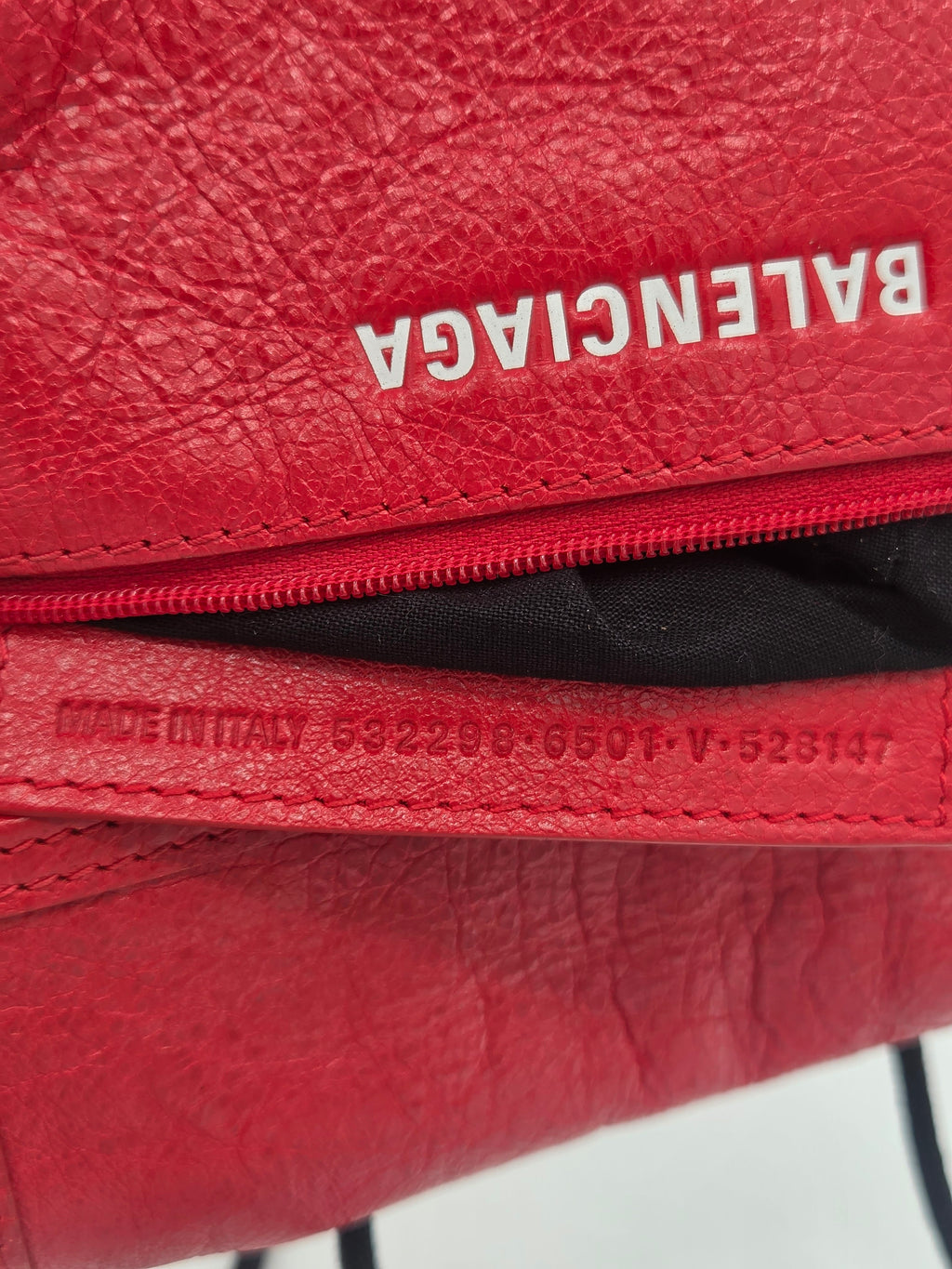 Close-up of a red textured leather zippered pouch with the Balenciaga logo printed vertically in white on the left side.