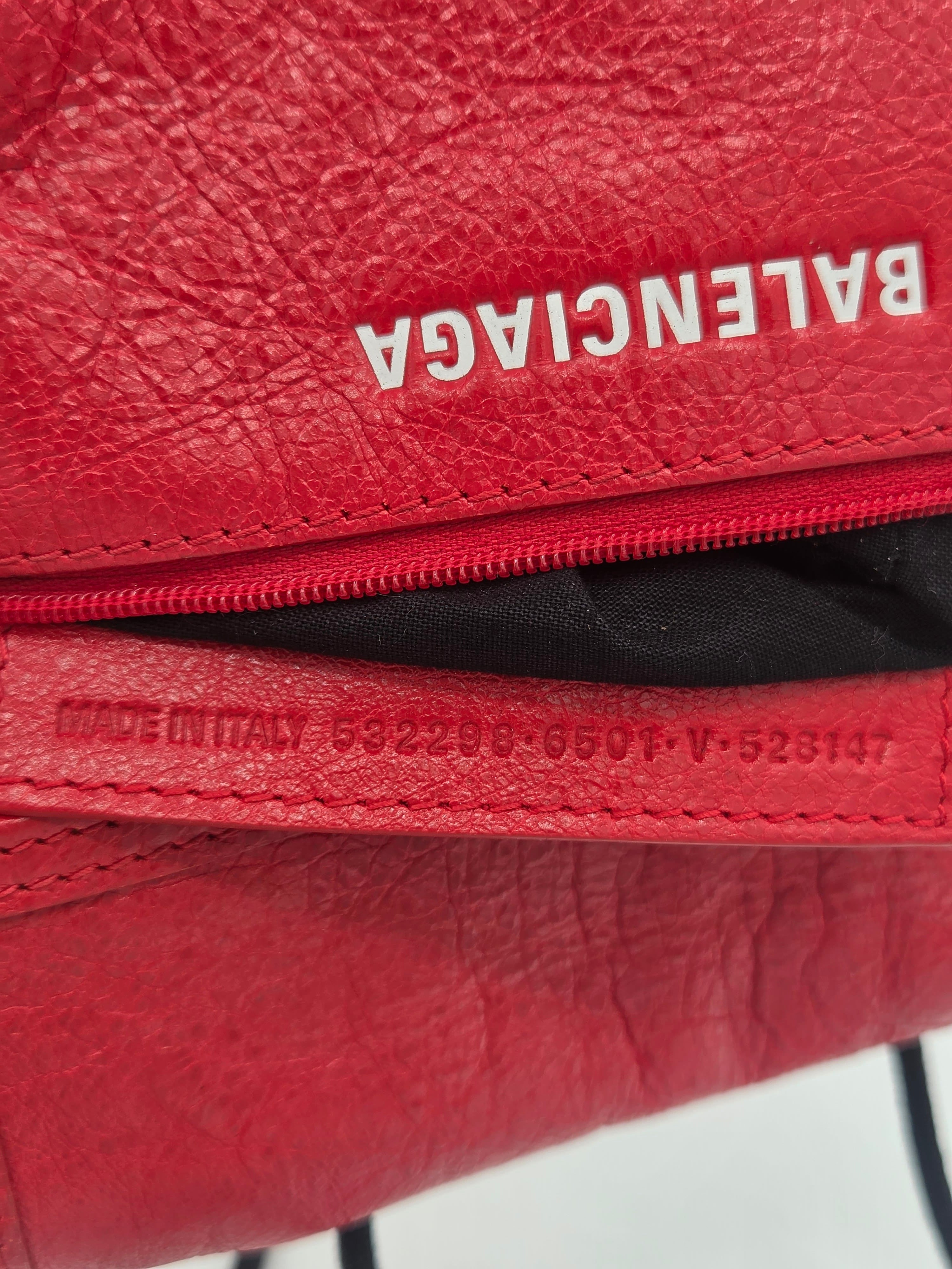 Close-up of a red textured leather zippered pouch with the Balenciaga logo printed vertically in white on the left side.
