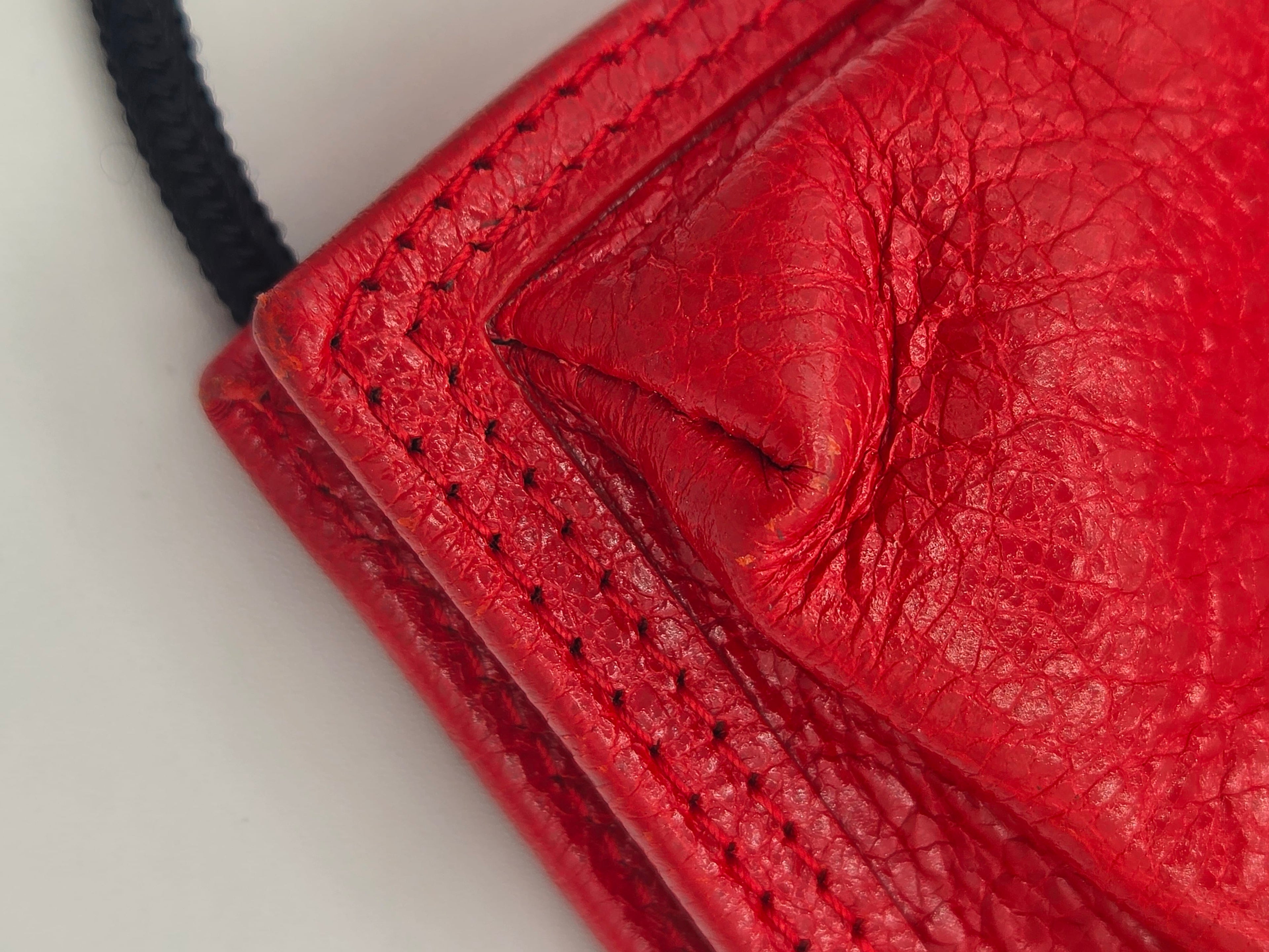 Close-up detail of a textured red leather product corner with visible stitching and a black cord against a light background.