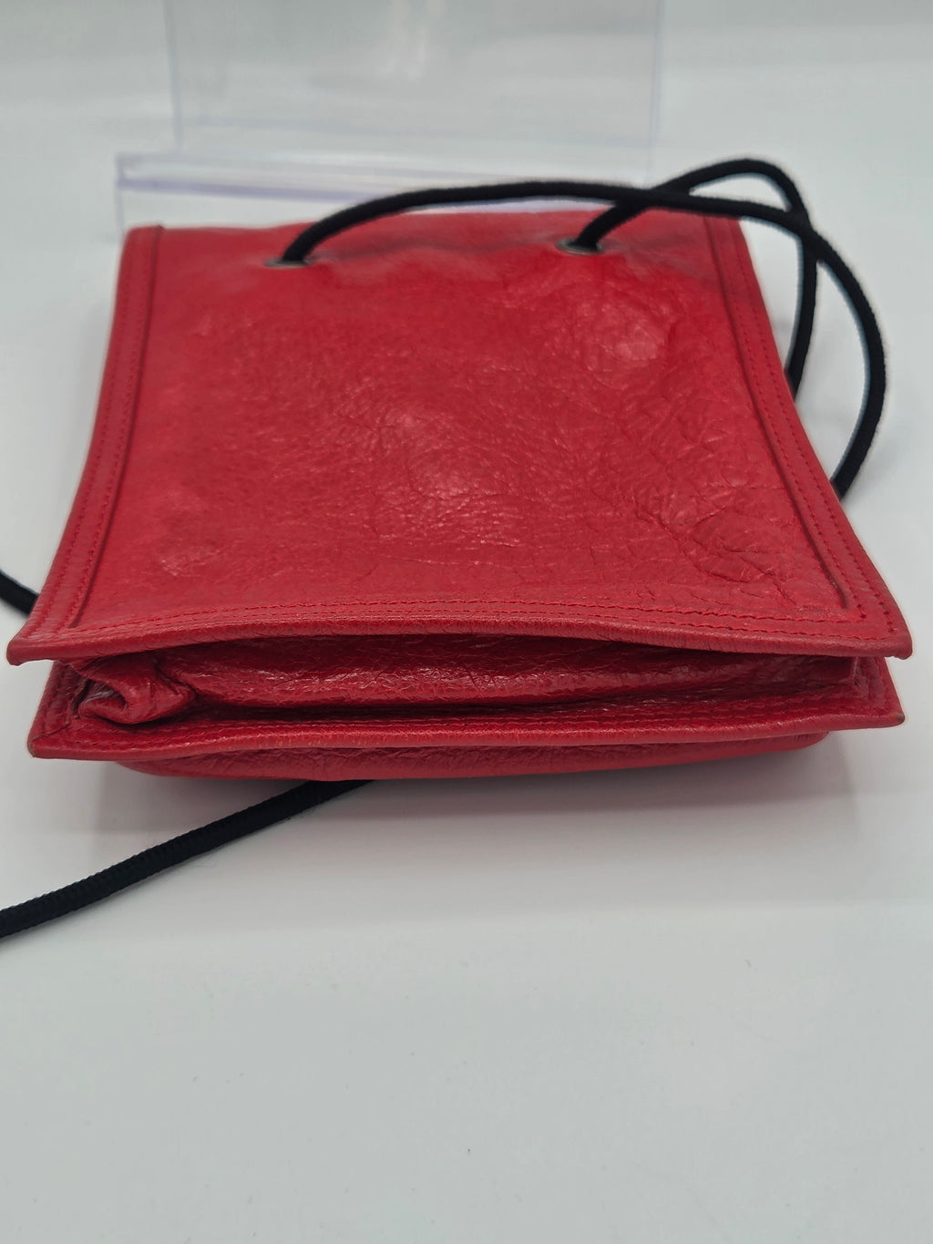 A red textured leather pouch bag with black drawstring cords, shown from a side angle against a plain white background.