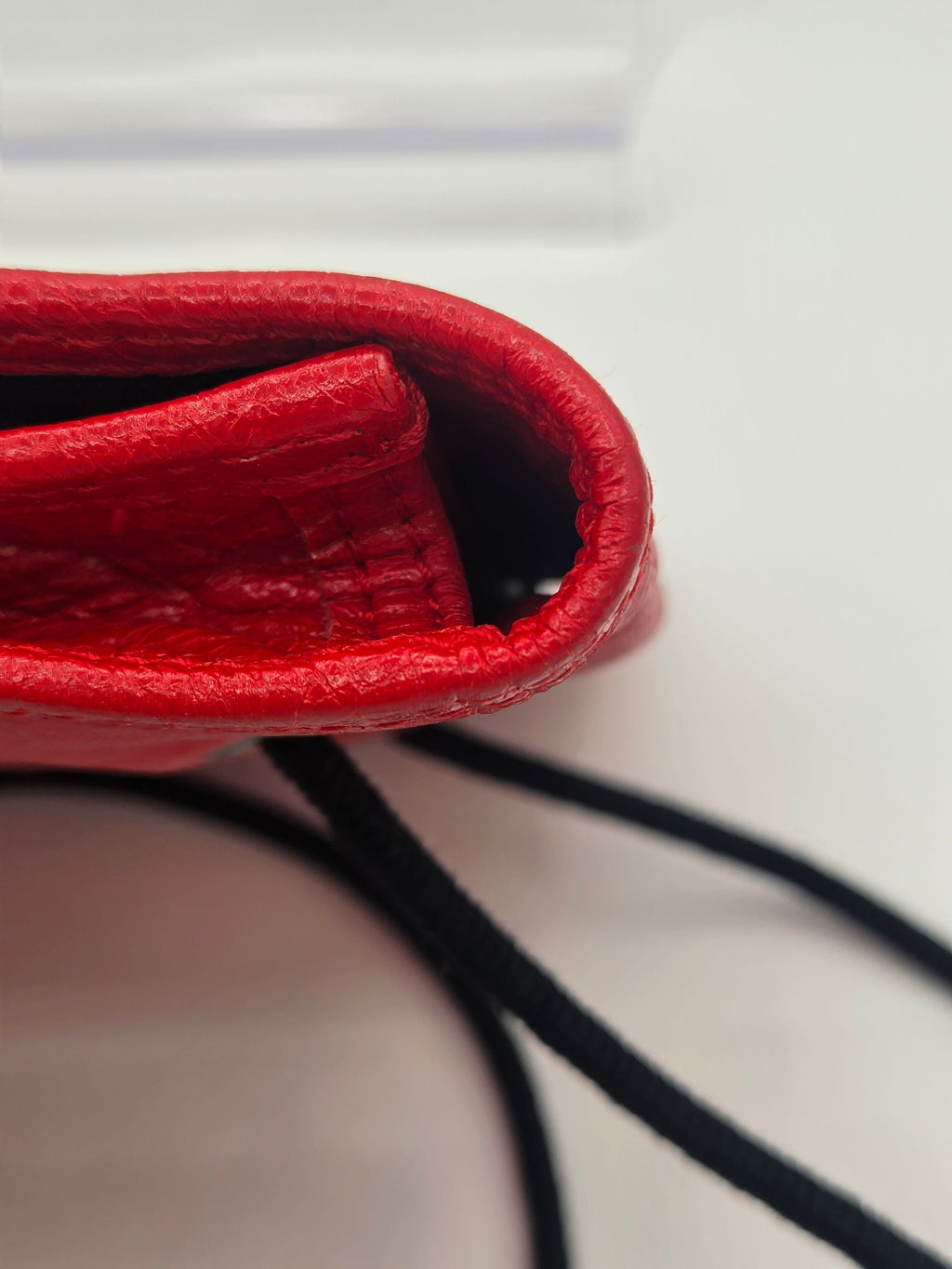 Close-up detail of a red textured leather bag corner with black drawstring cords against a light neutral background.