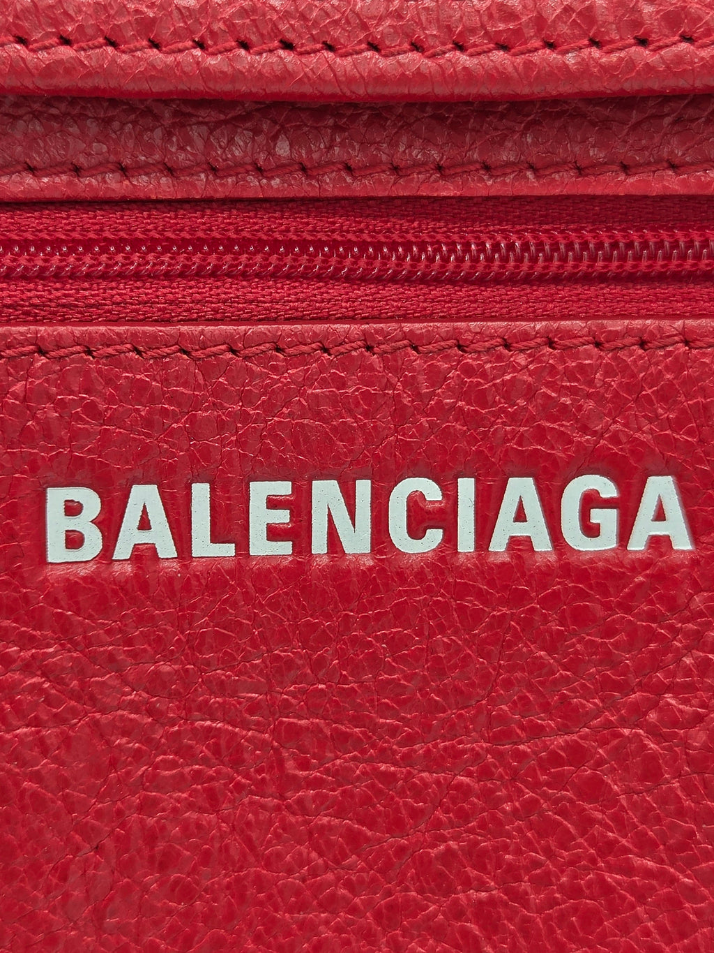 Close-up of a red textured leather wallet or card holder with a vertical white BALENCIAGA logo printed on the front.