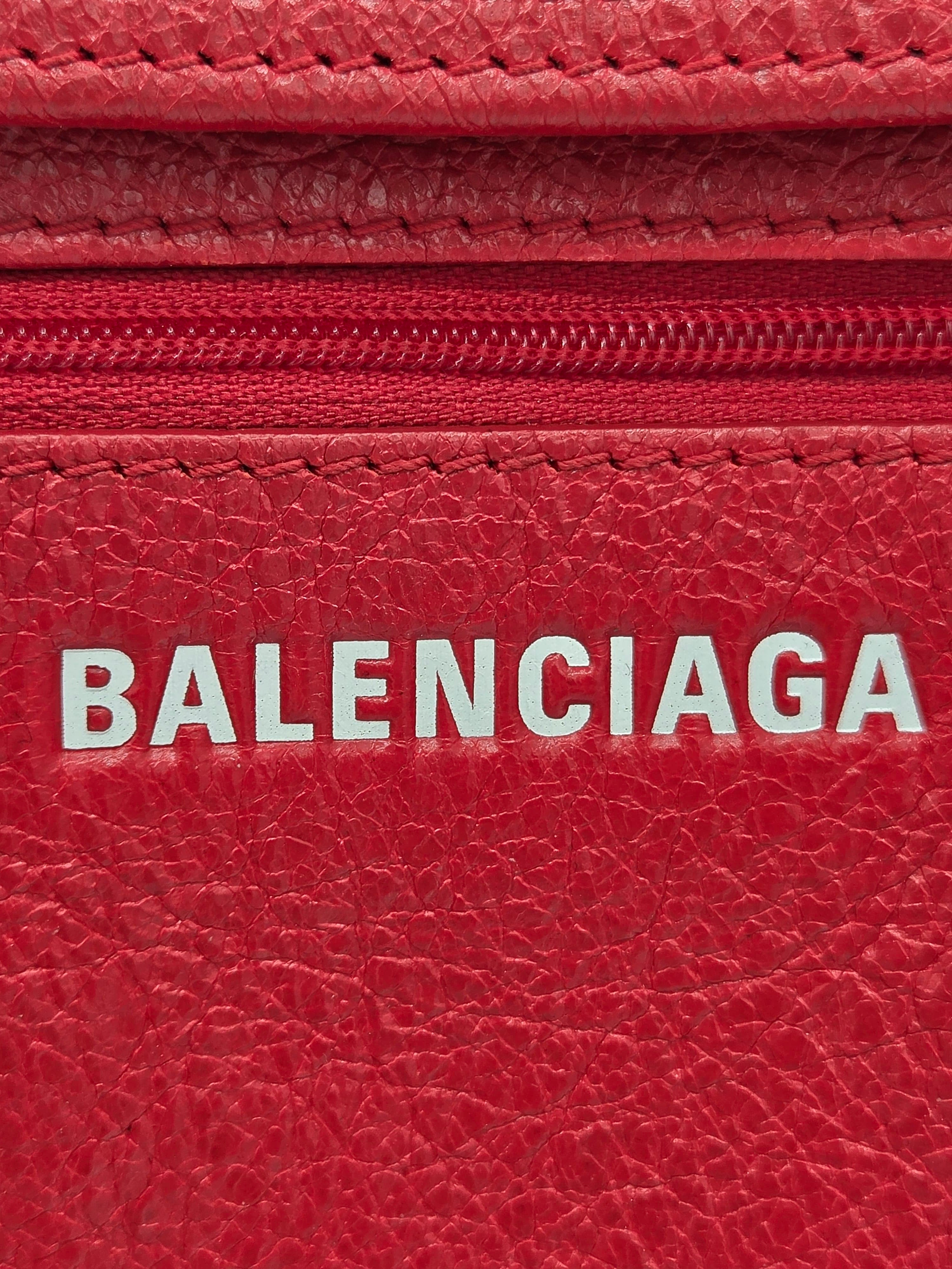 Close-up of a red textured leather wallet or card holder with a vertical white BALENCIAGA logo printed on the front.