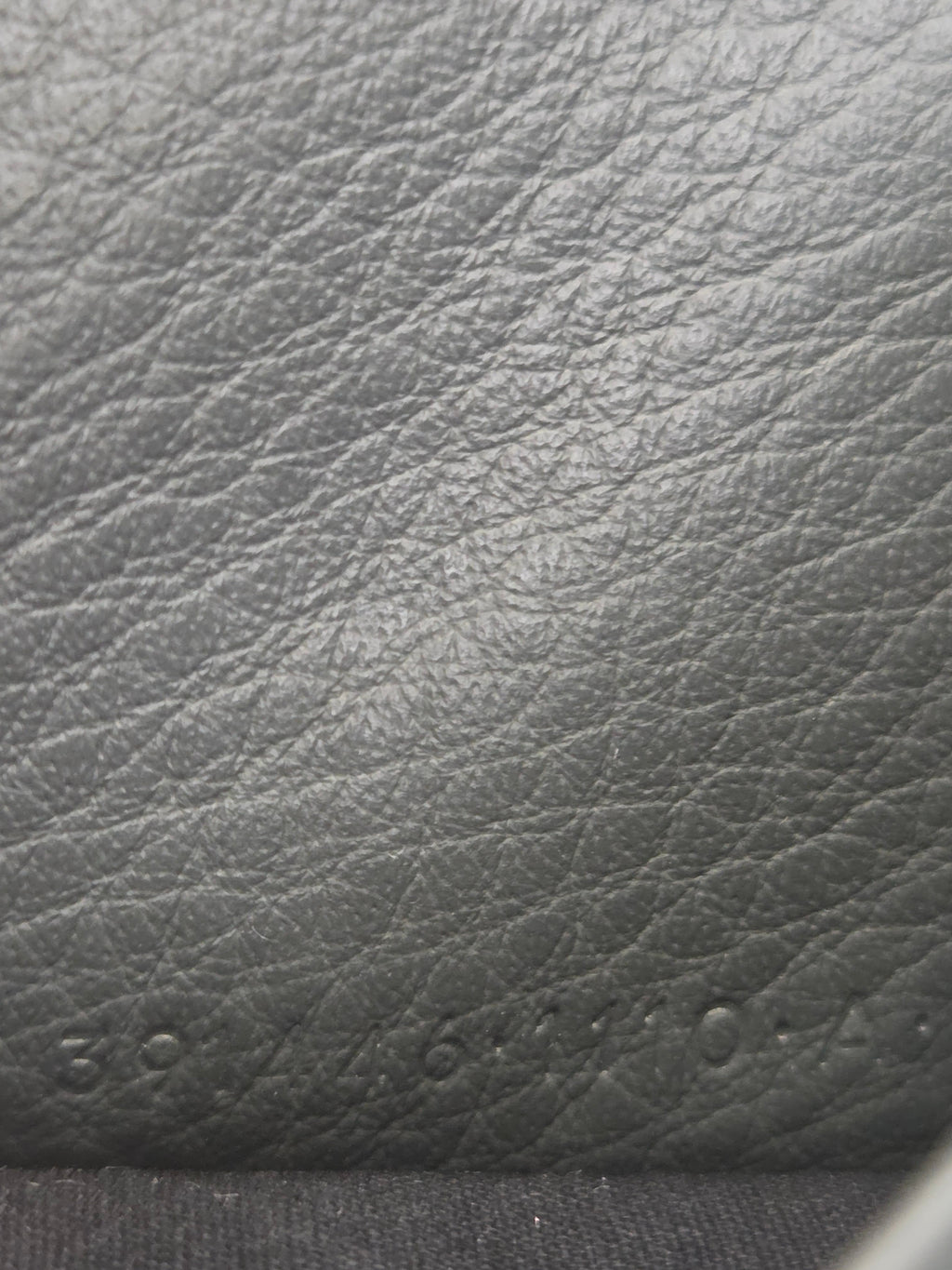 Close-up of a dark gray textured leather surface with visible grain and a stitched edge on the right.