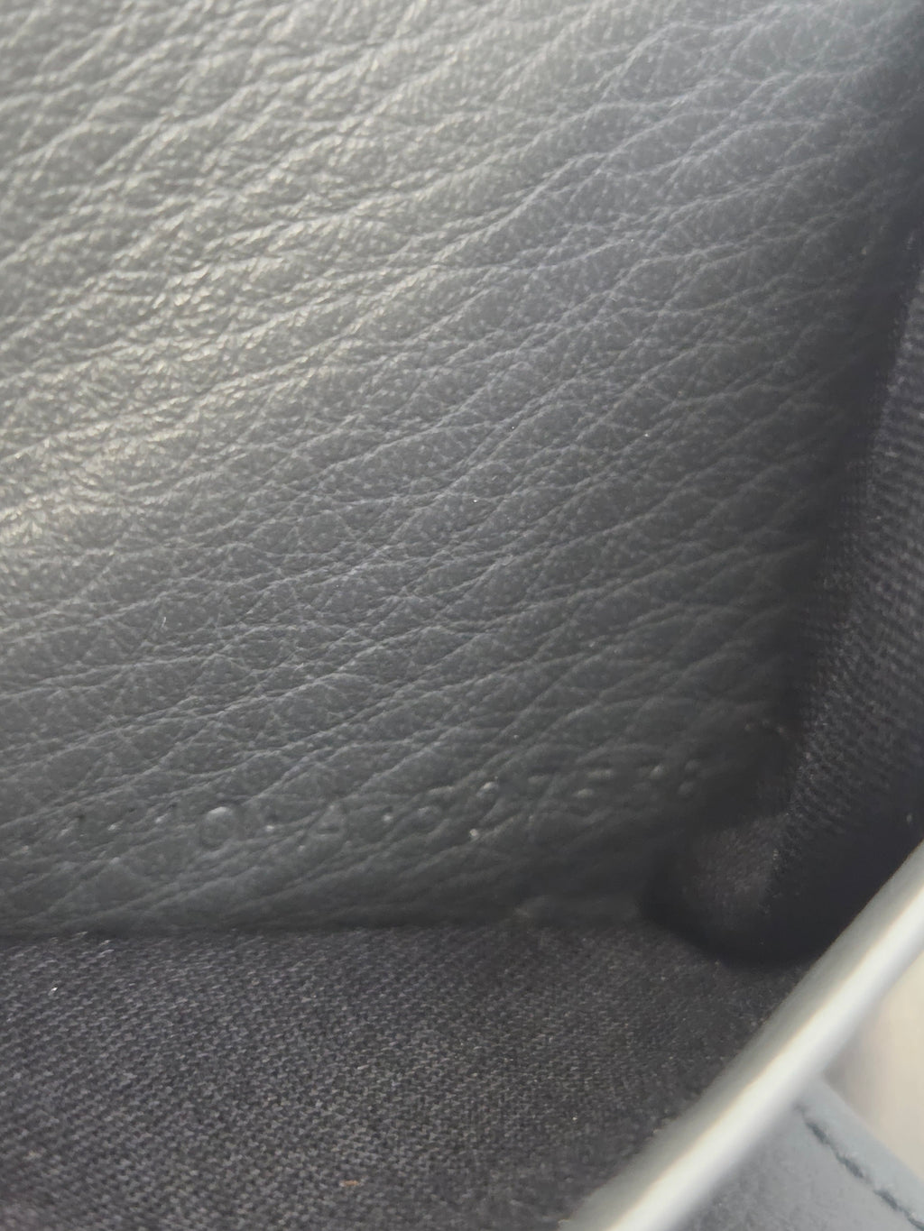 Close-up of a dark gray pebbled leather surface next to a black woven fabric and a light gray trim edge.