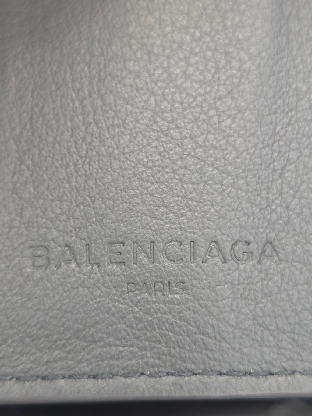 Close-up of a light gray pebbled leather surface with vertically embossed Balenciaga Paris branding.