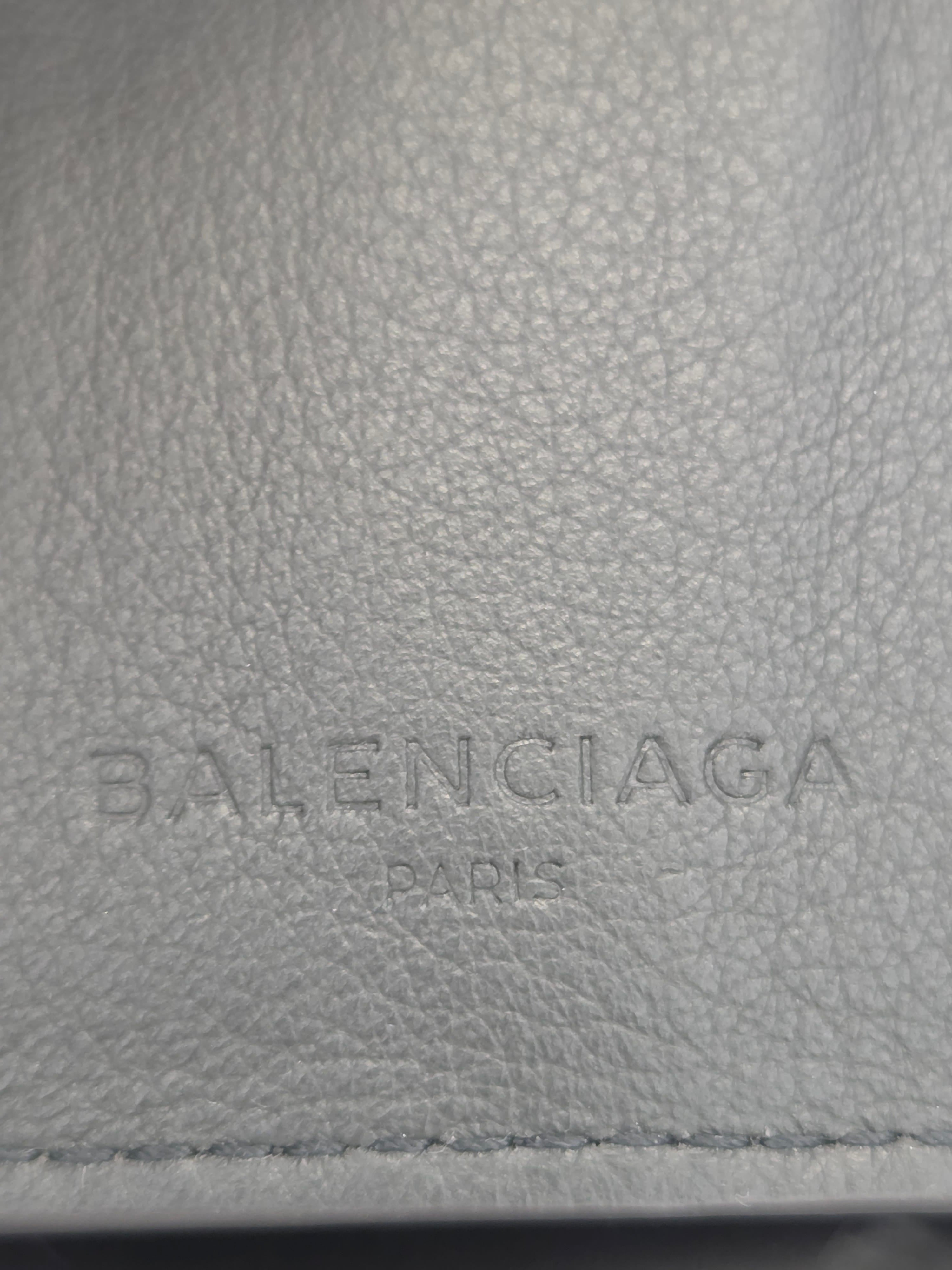 Close-up of a light gray pebbled leather surface with vertically embossed Balenciaga Paris branding.