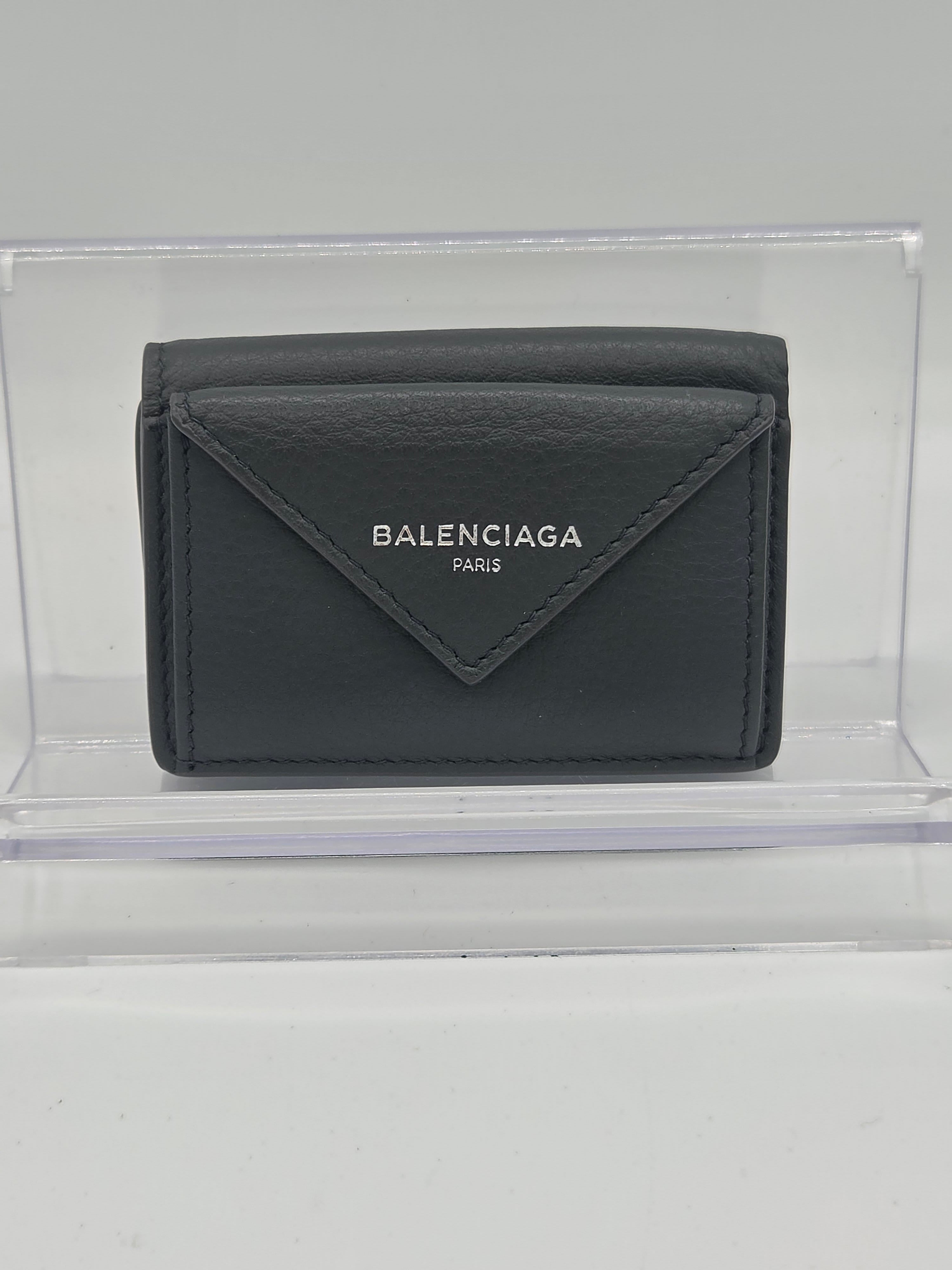 A dark gray Balenciaga leather wallet displayed inside a clear acrylic block on a light gray background.