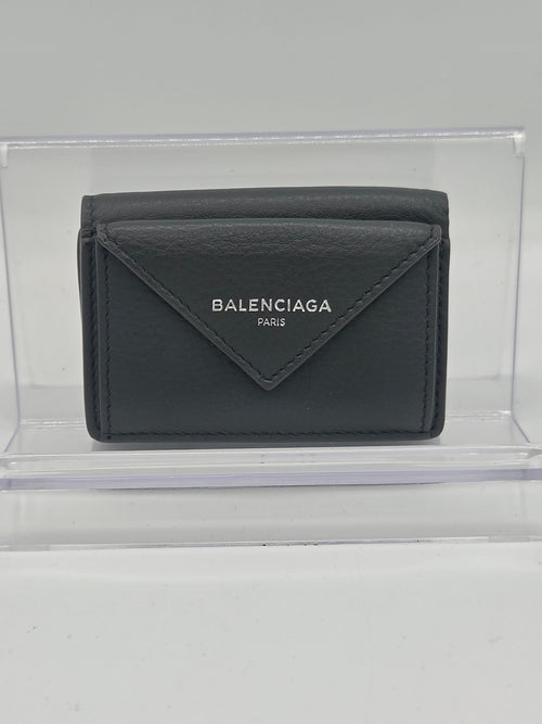 A dark gray Balenciaga leather wallet displayed inside a clear acrylic block on a light gray background.