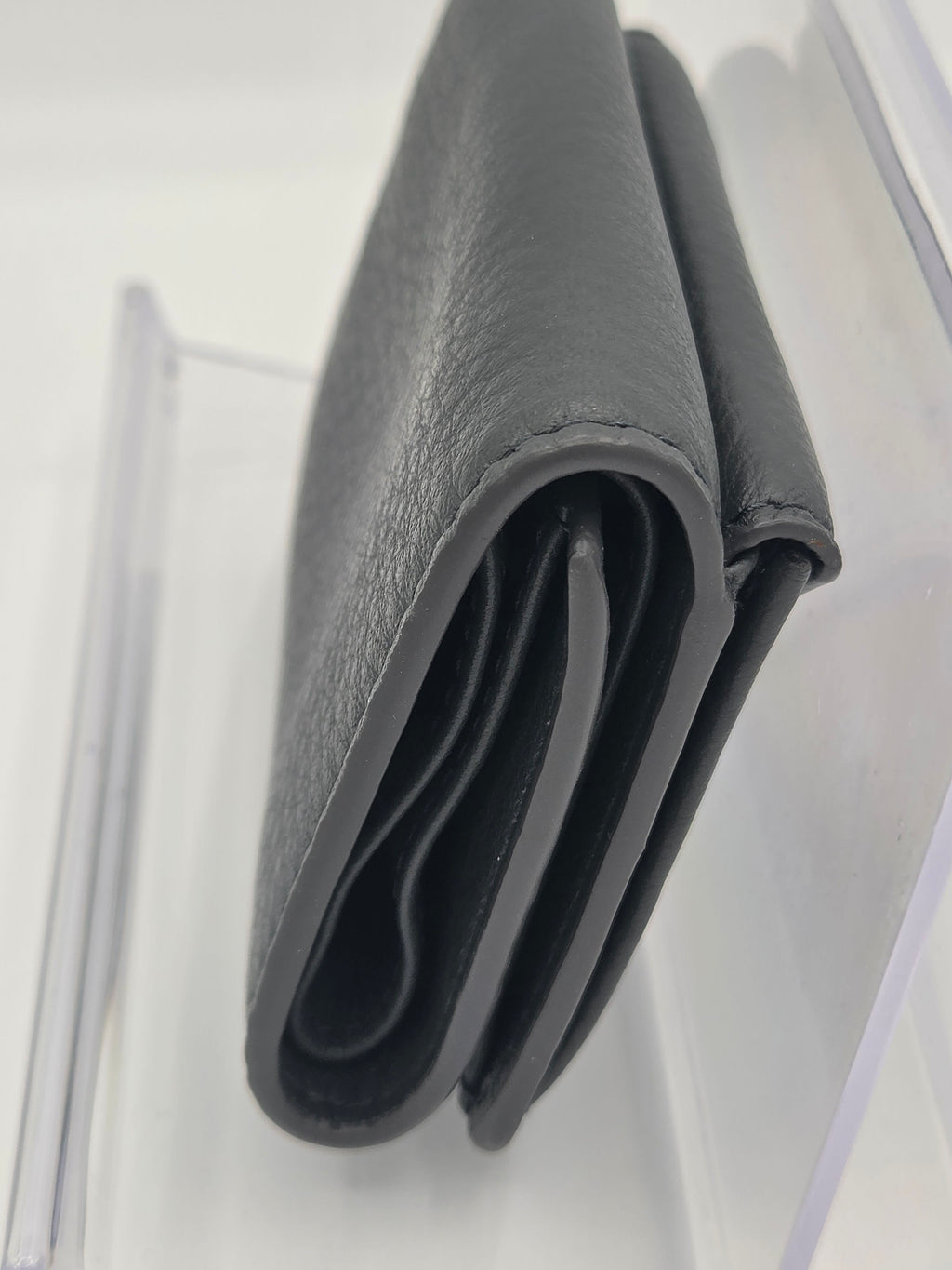 A close-up of a dark gray pebbled leather wallet, folded to show its interior card slots, resting on a clear acrylic surface.