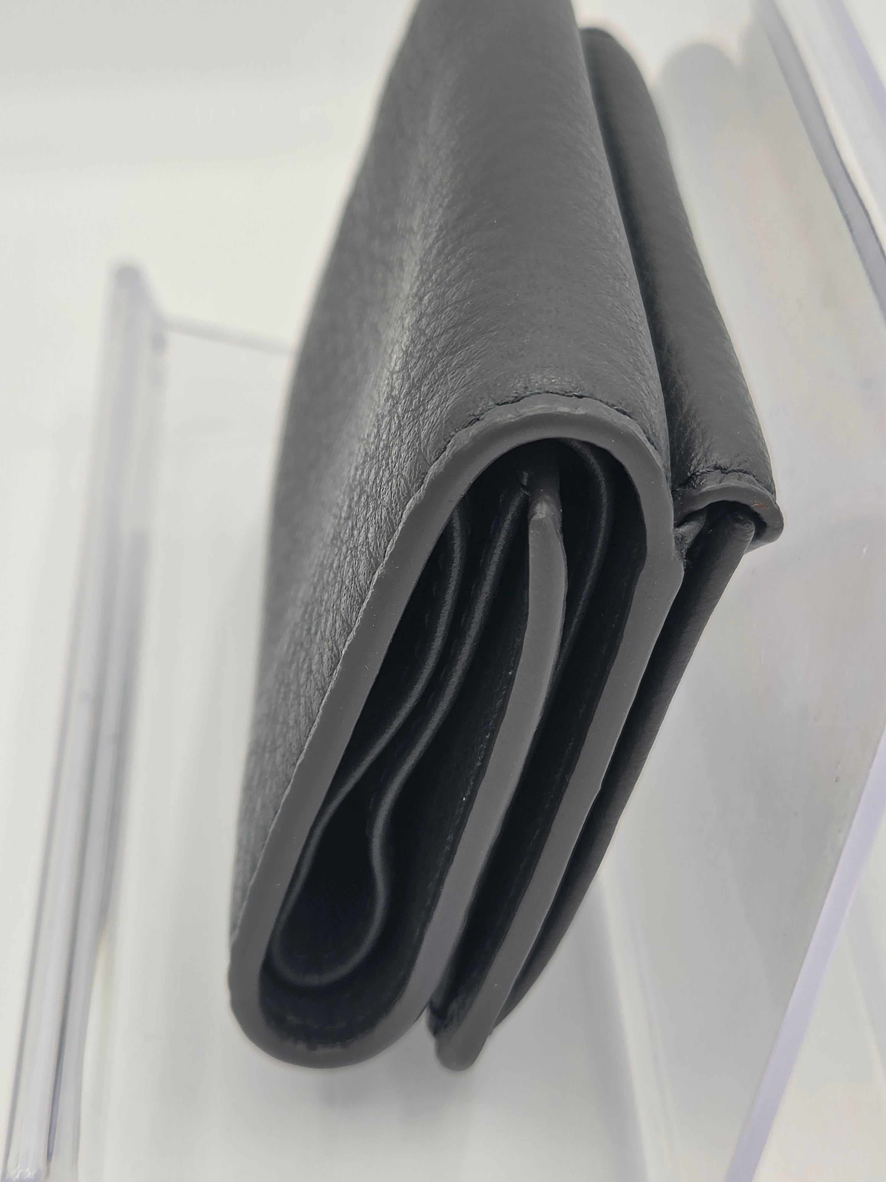 A close-up of a dark gray pebbled leather wallet, folded to show its interior card slots, resting on a clear acrylic surface.