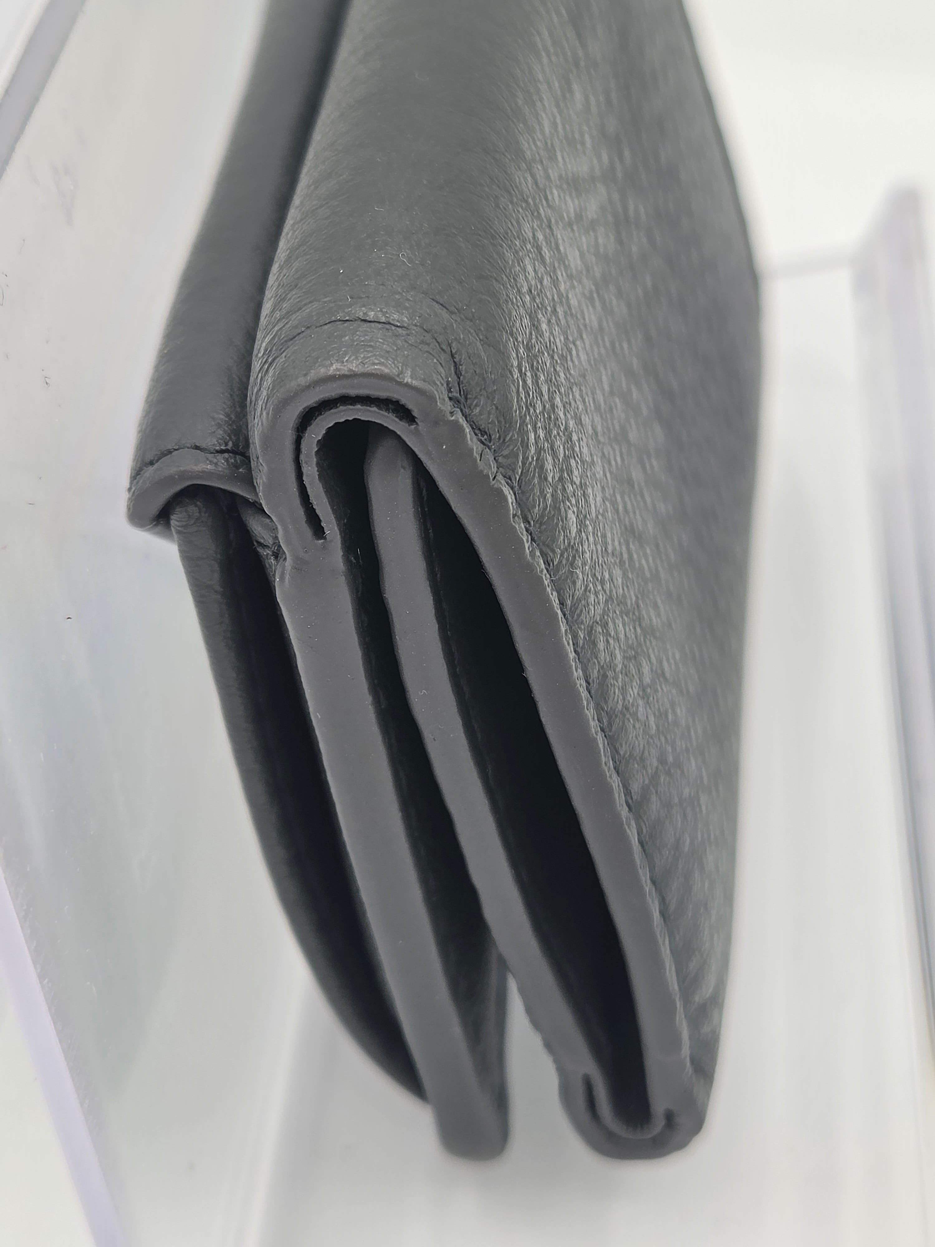 A dark gray textured leather bifold wallet folded neatly on a clear acrylic surface.