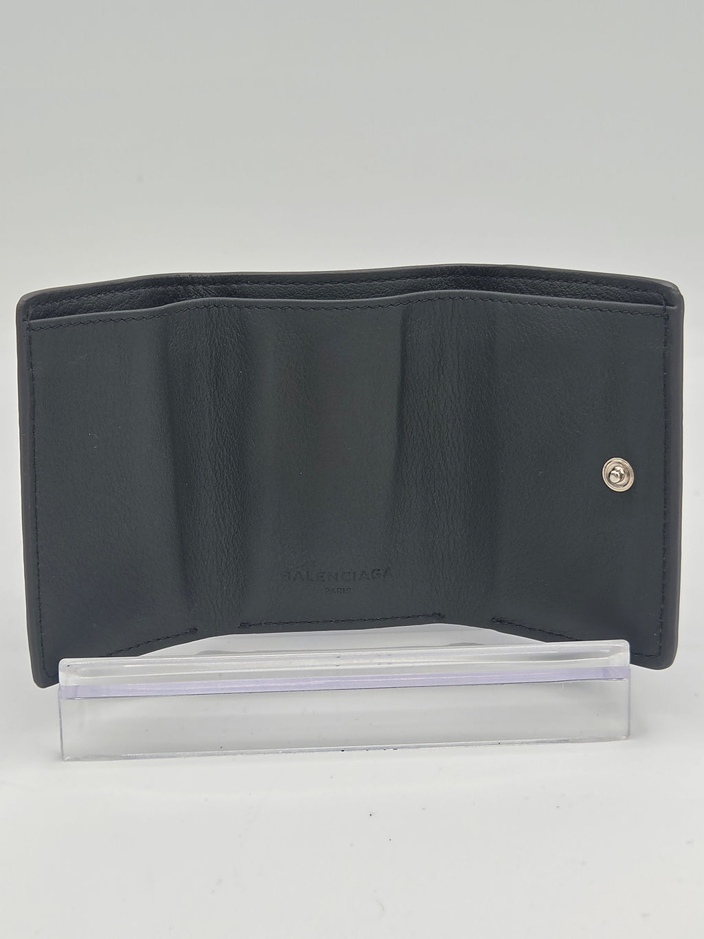 A black leather wallet with a silver snap button closure, shown open next to a clear plastic sleeve on a plain white background.