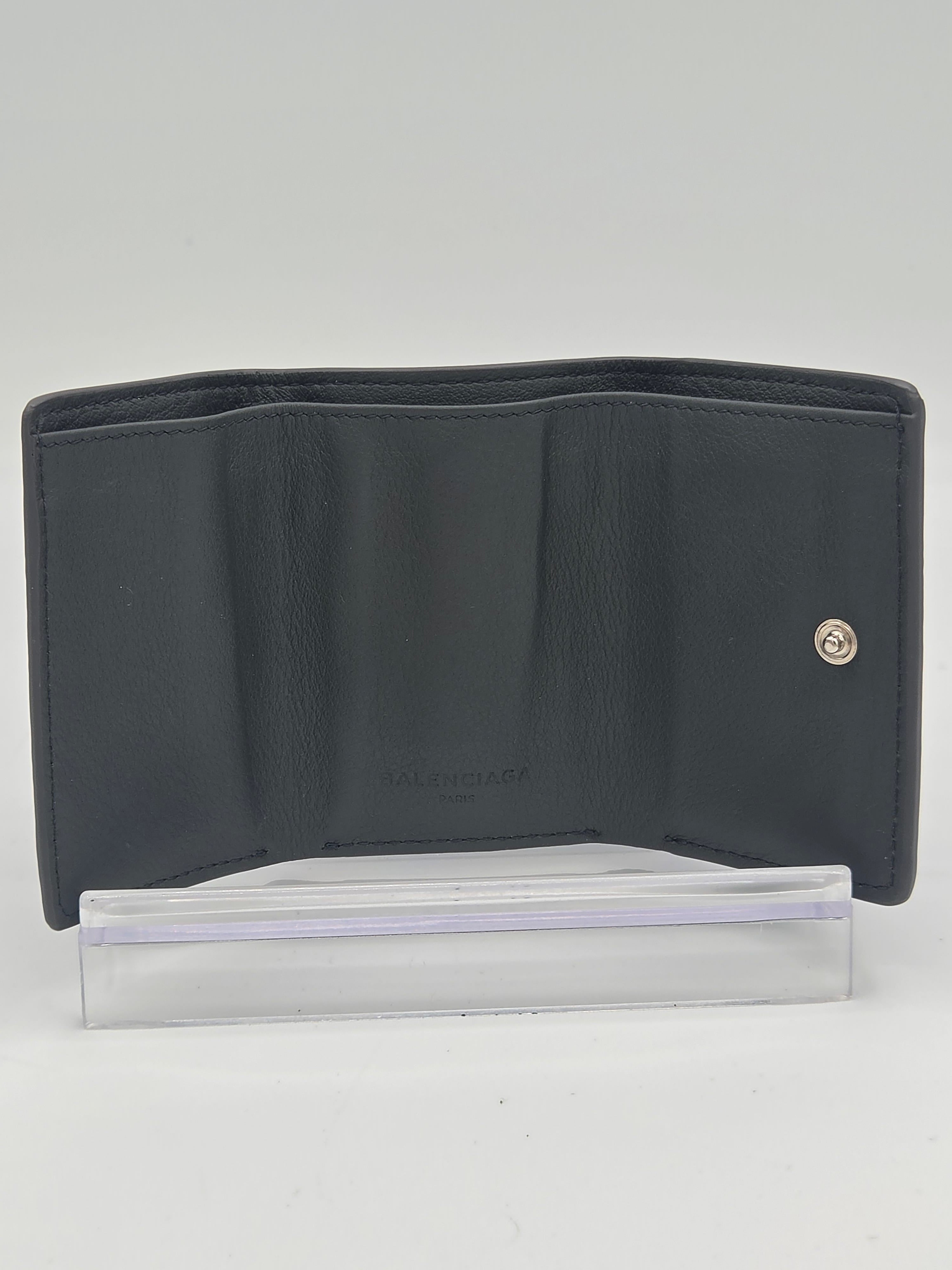 A black leather wallet with a silver snap button closure, shown open next to a clear plastic sleeve on a plain white background.