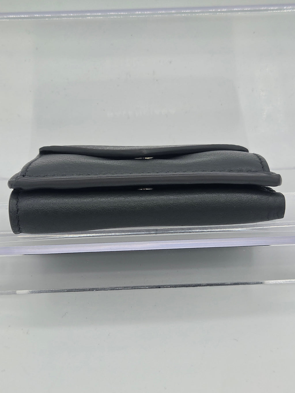 A dark gray leather sleeve or pouch shown vertically inside a clear plastic display case against a light gray background.