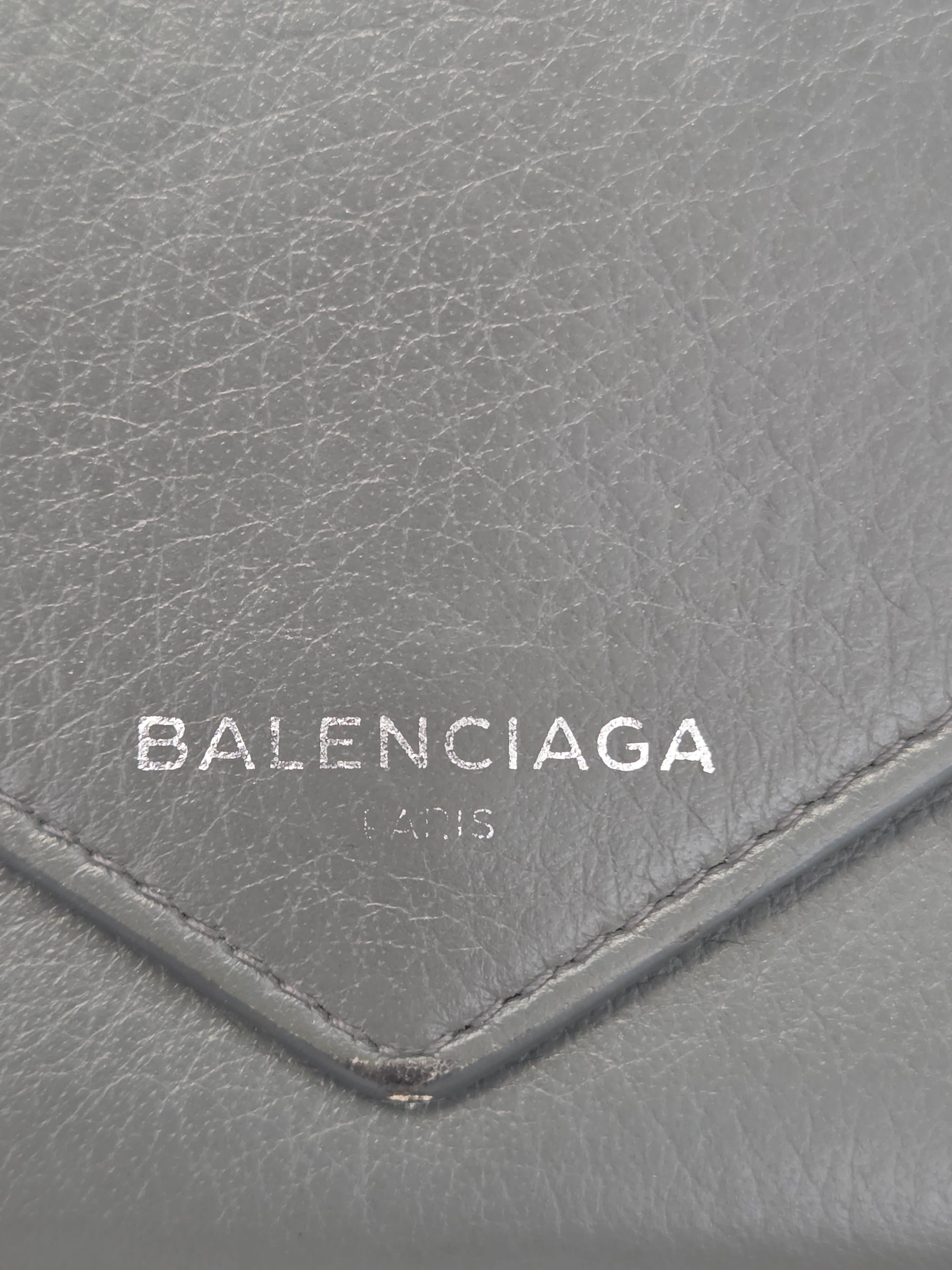 Close-up of a gray textured leather wallet or pouch with a stitched chevron detail and vertical white Balenciaga Paris branding.