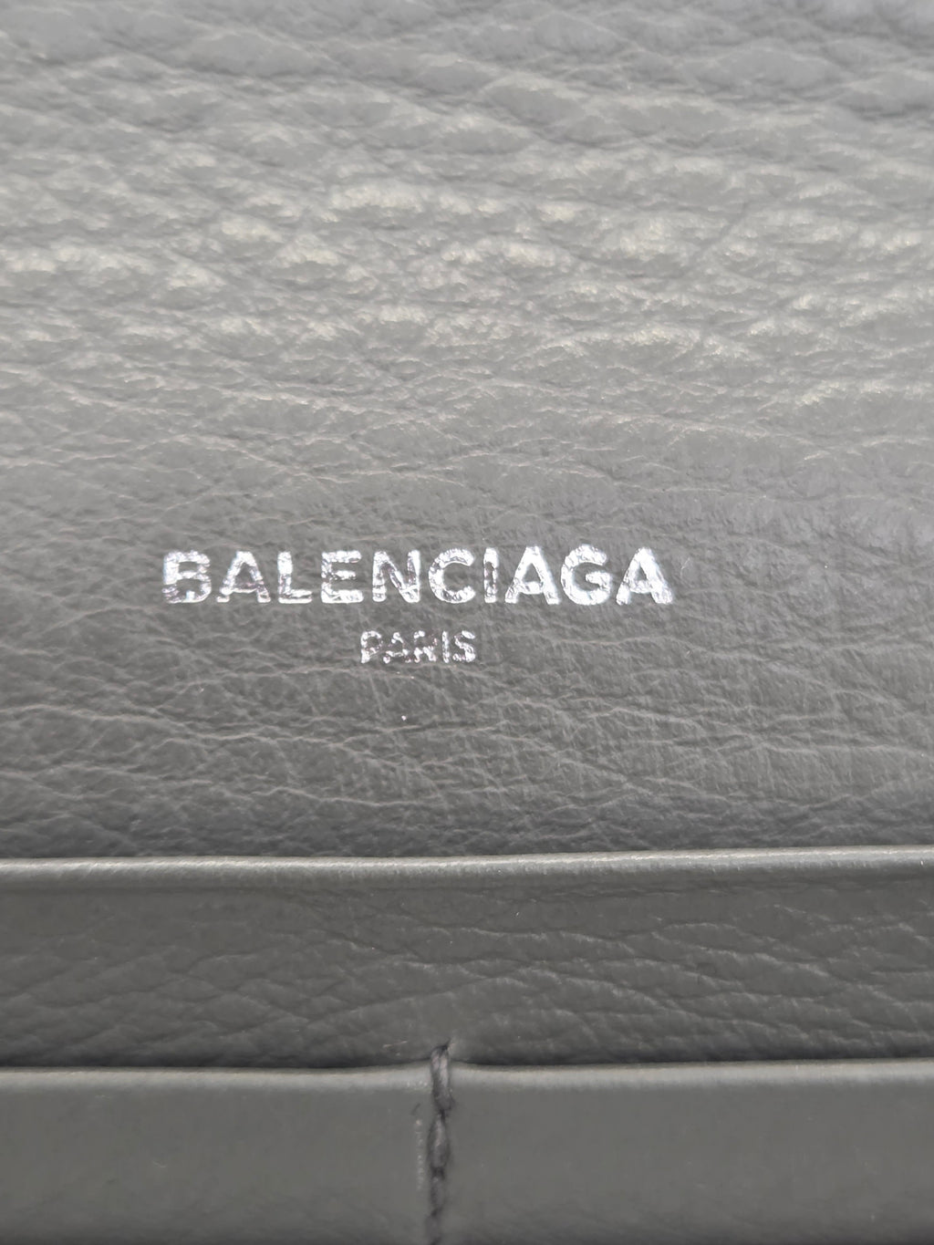 Close-up of a gray textured leather surface with the Balenciaga Paris logo printed vertically in white.