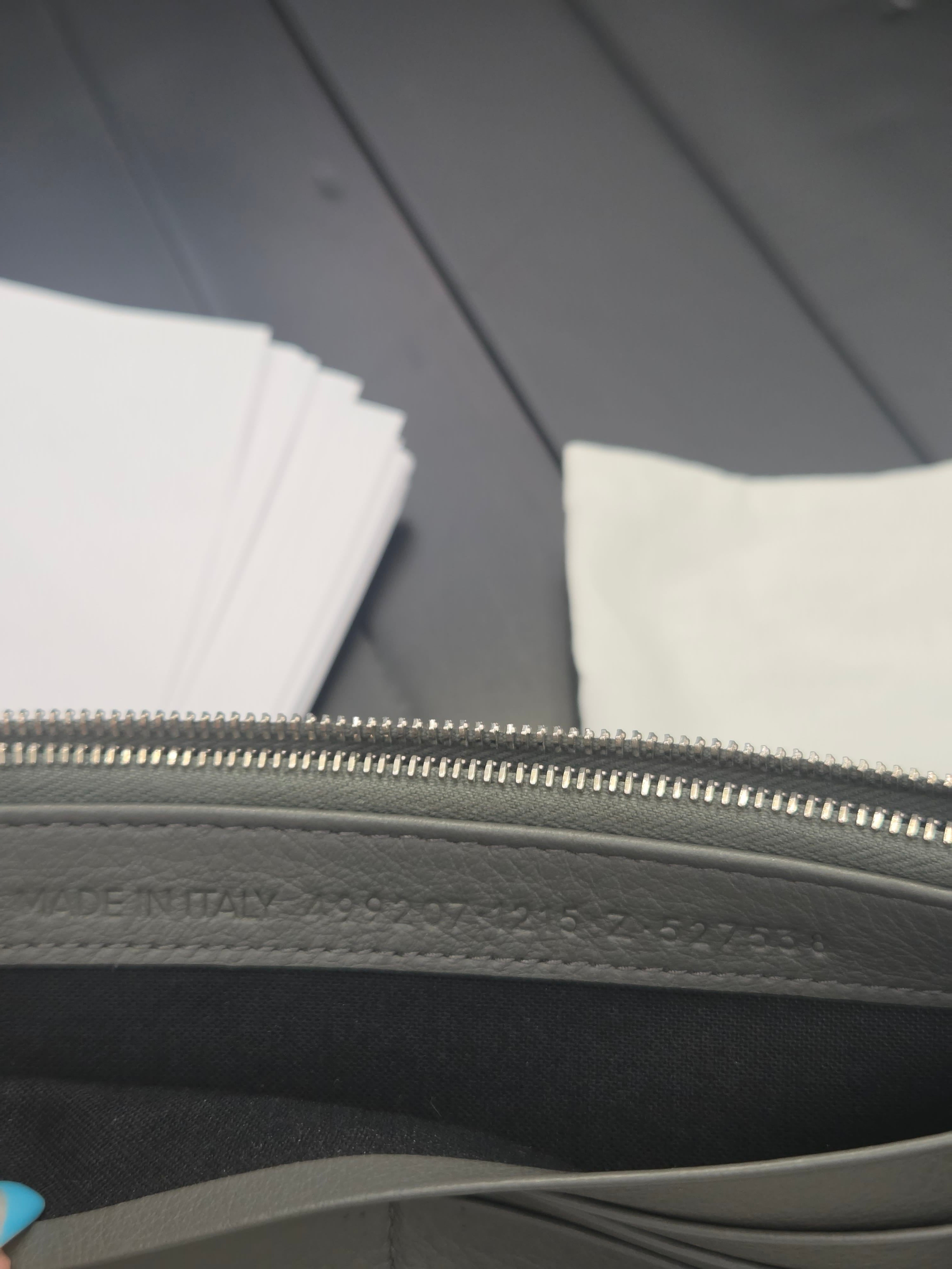 Close-up detail of a dark gray leather zipper pouch with a silver metal zipper, showing the 'MADE IN ITALY' embossing on the leather trim.