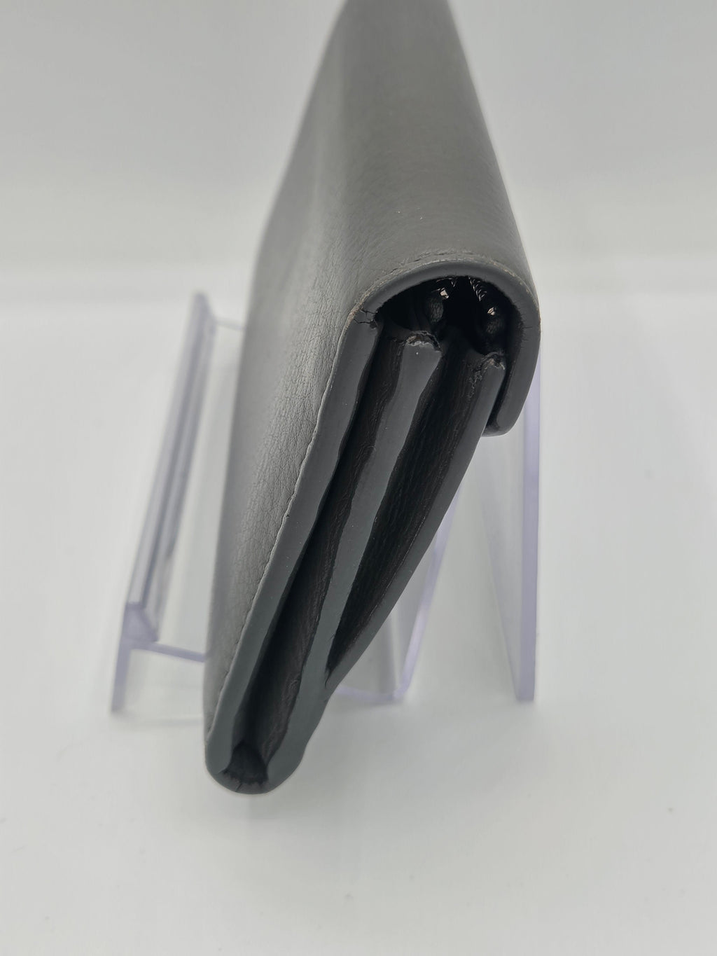 A close-up of a gray leather or faux-leather accessory, possibly a sleeve or cover, shown from the side with a black interior lining and a clear acrylic display stand against a white background.