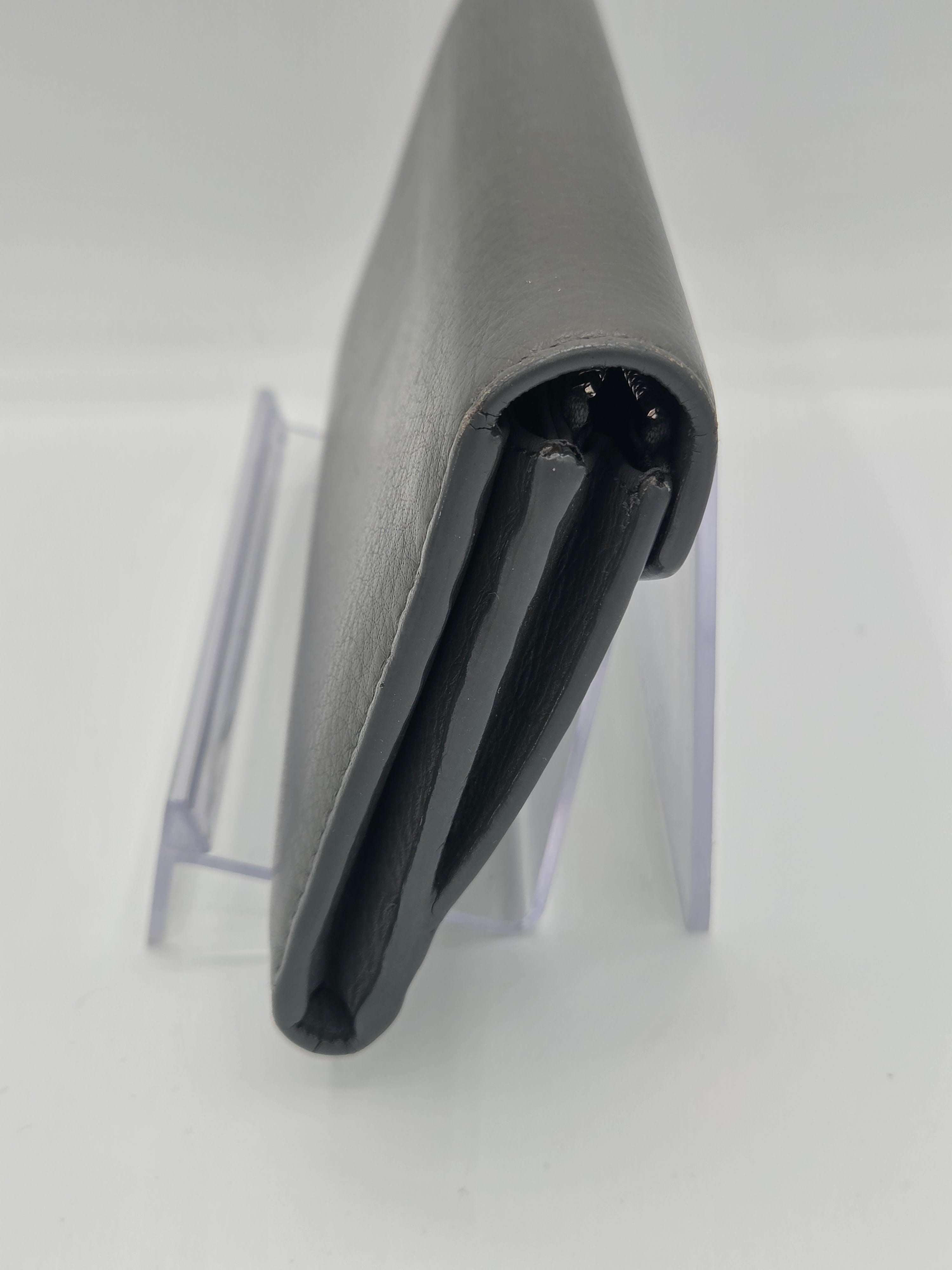 A close-up of a gray leather or faux-leather accessory, possibly a sleeve or cover, shown from the side with a black interior lining and a clear acrylic display stand against a white background.