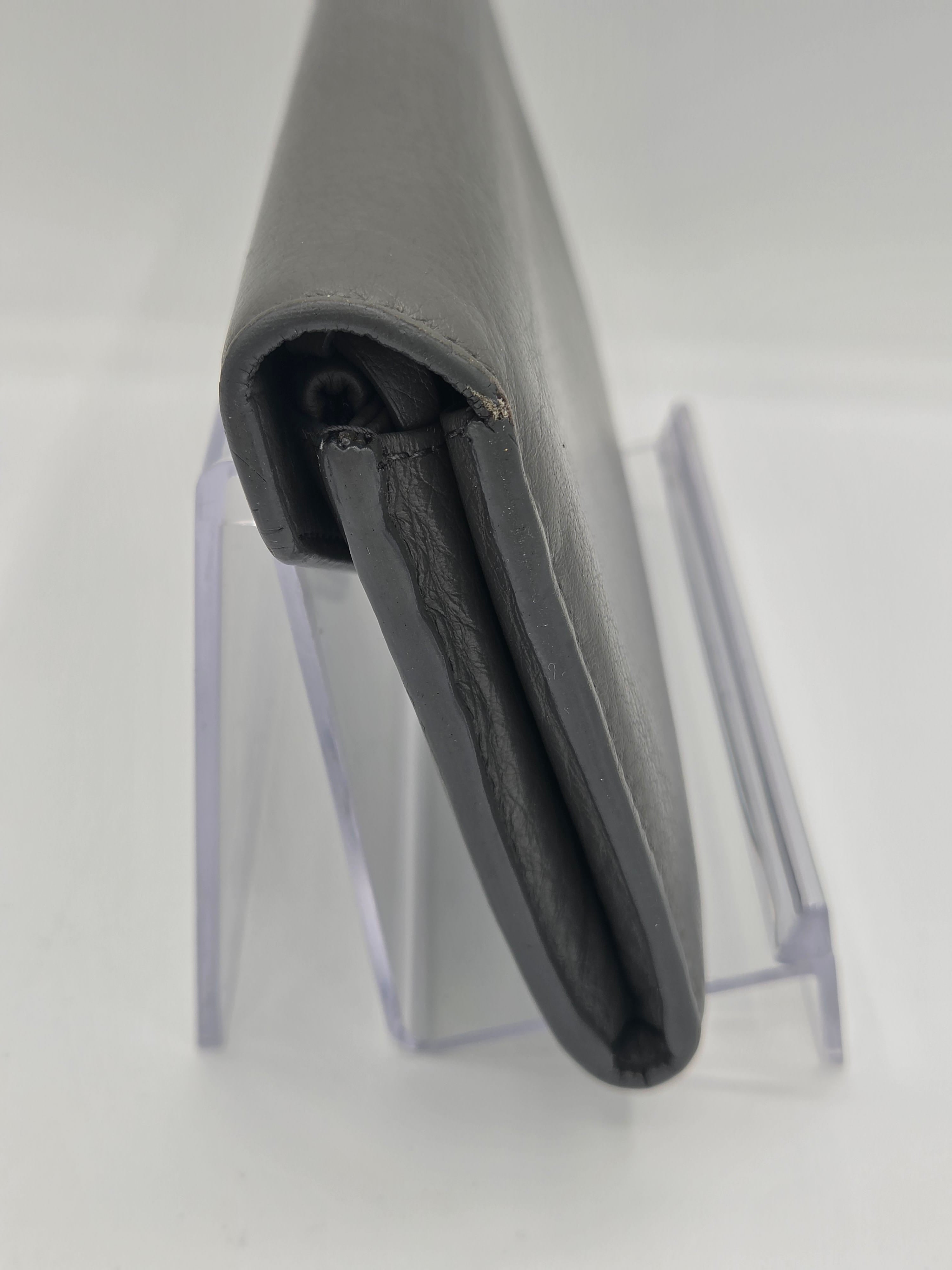 A dark gray leather wallet shown folded, resting on a clear acrylic display stand against a plain white background.