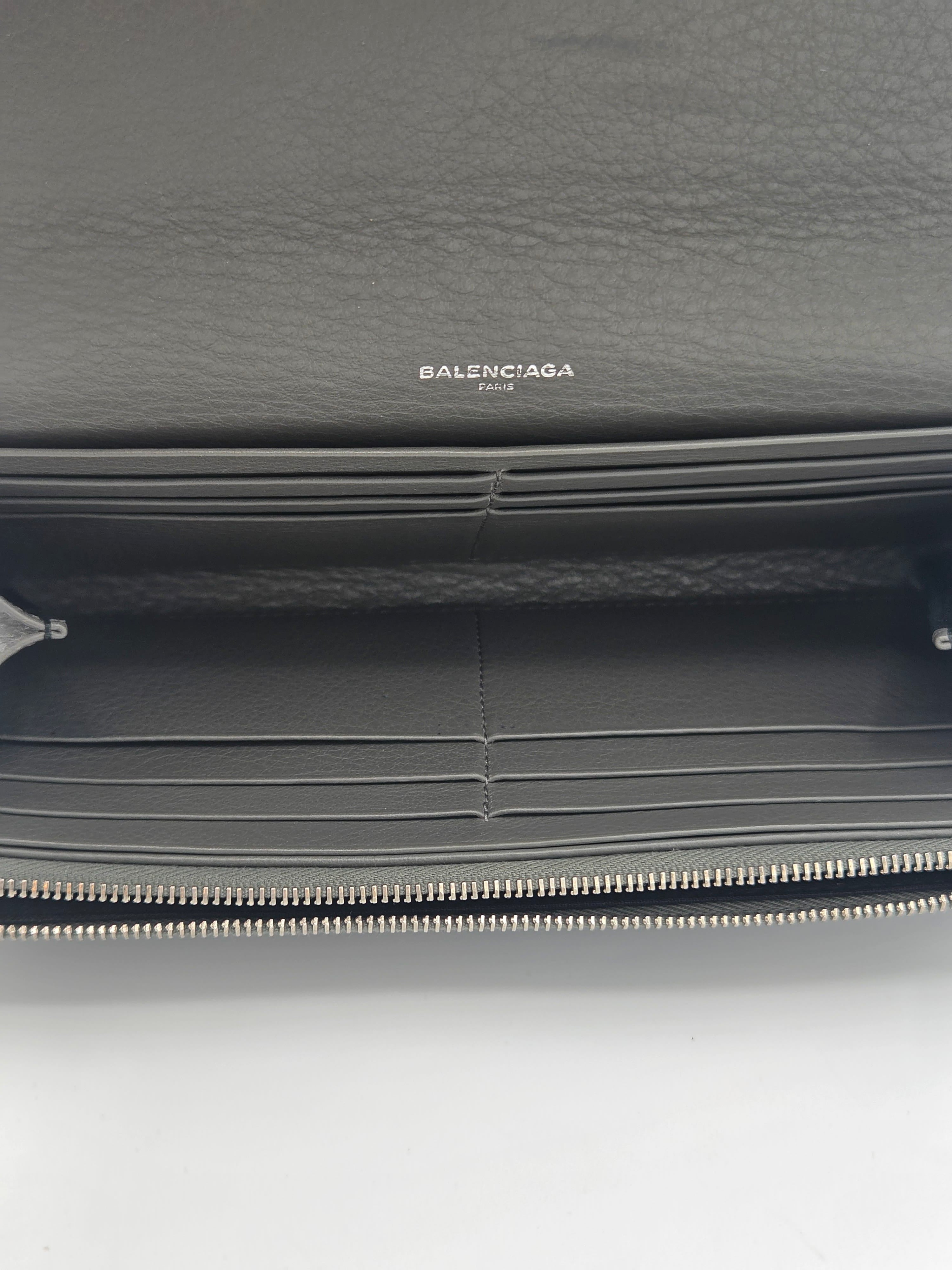 Close-up of a dark gray Balenciaga zip-around wallet showing the interior card slots, textured leather exterior, and silver zipper.