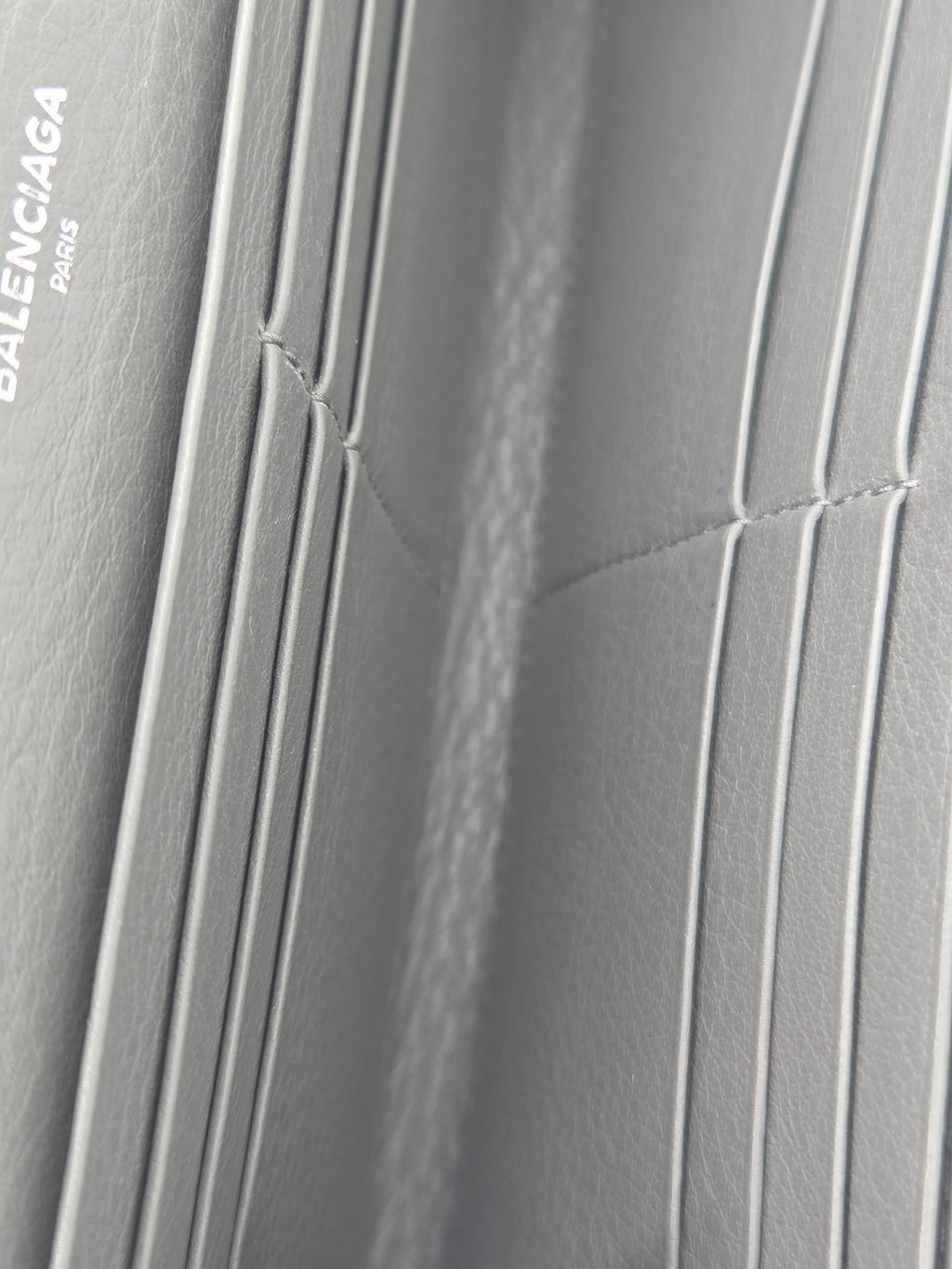 Close-up of a light gray textured leather interior with multiple card slots and a small visible Balenciaga logo near the bottom.
